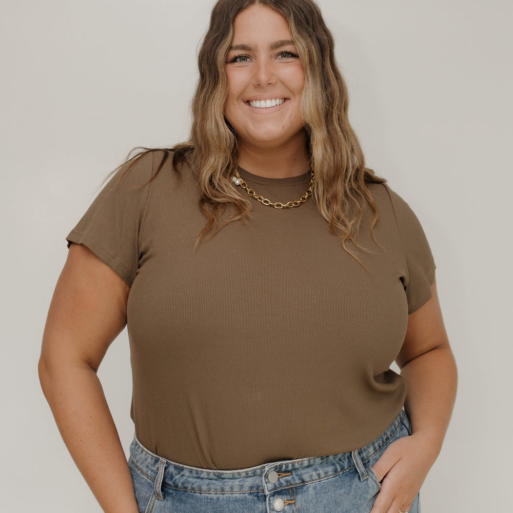 Woman wearing a brown t-shirt and blue jeans against a white background