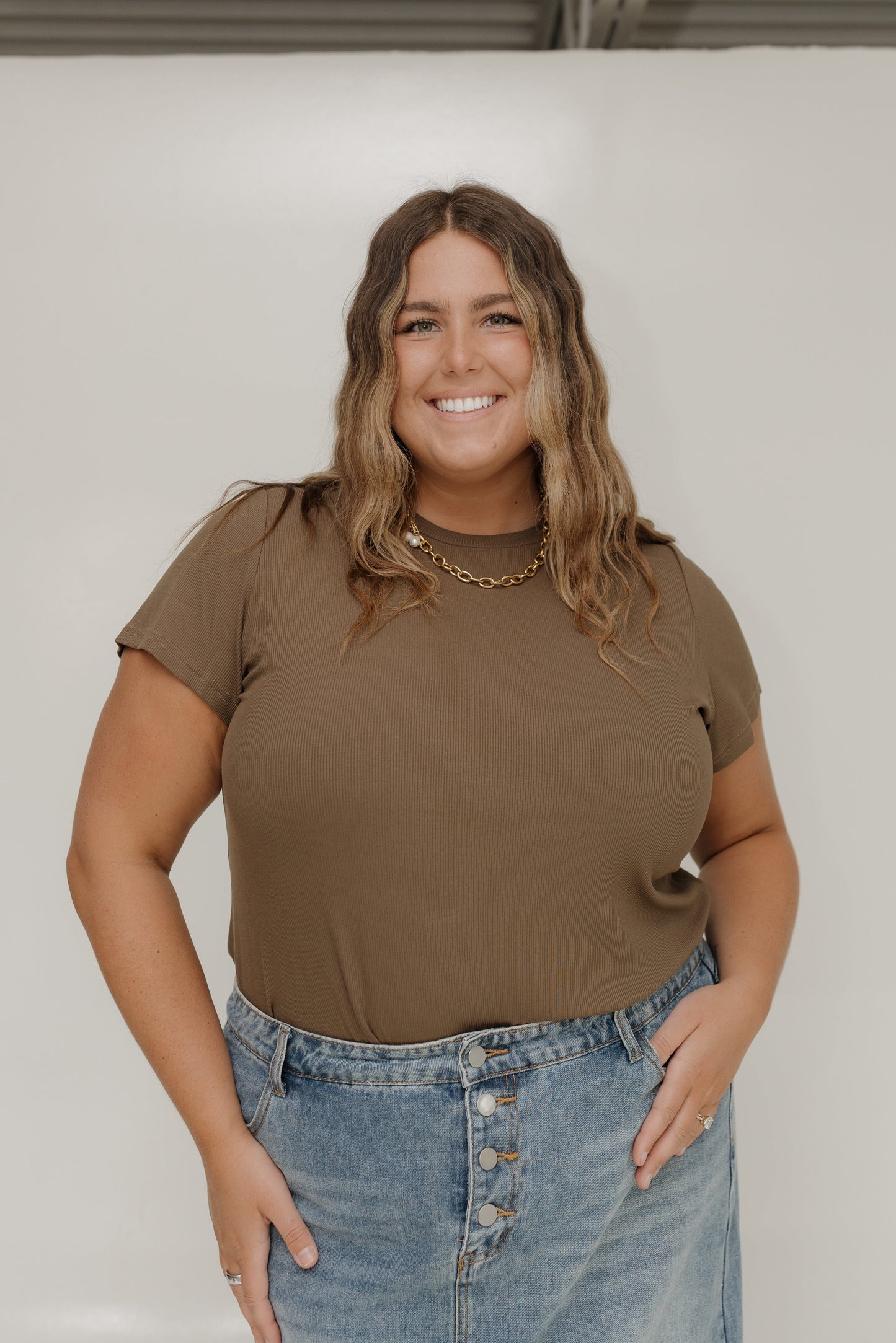 Woman wearing a brown t-shirt and blue jeans against a white background