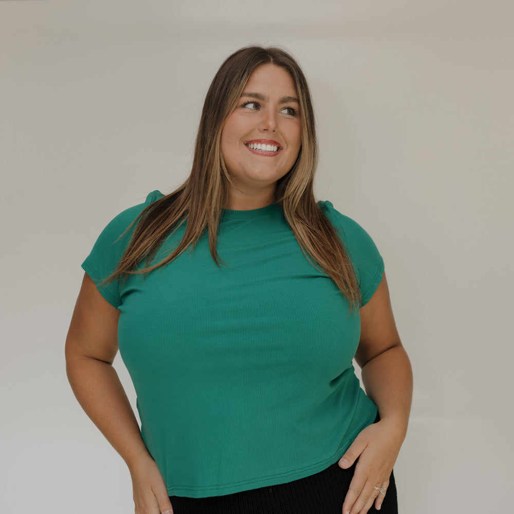 Woman wearing a green top against a white wall