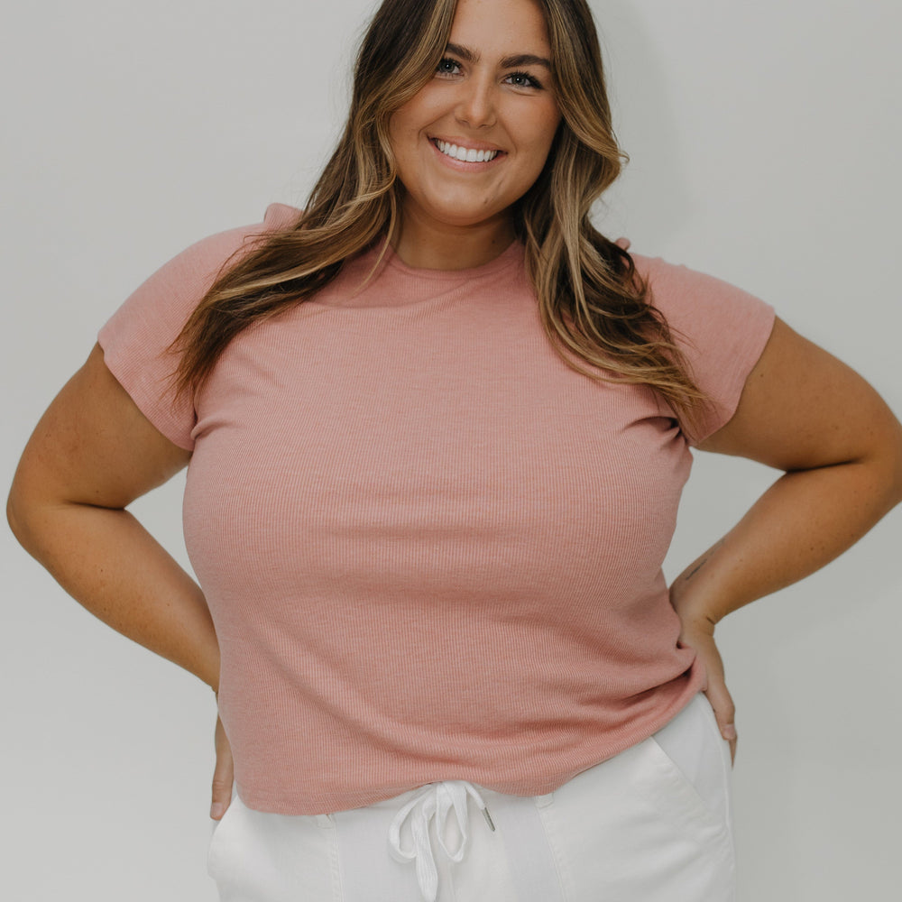 Woman wearing a pink t-shirt and white pants against a plain background