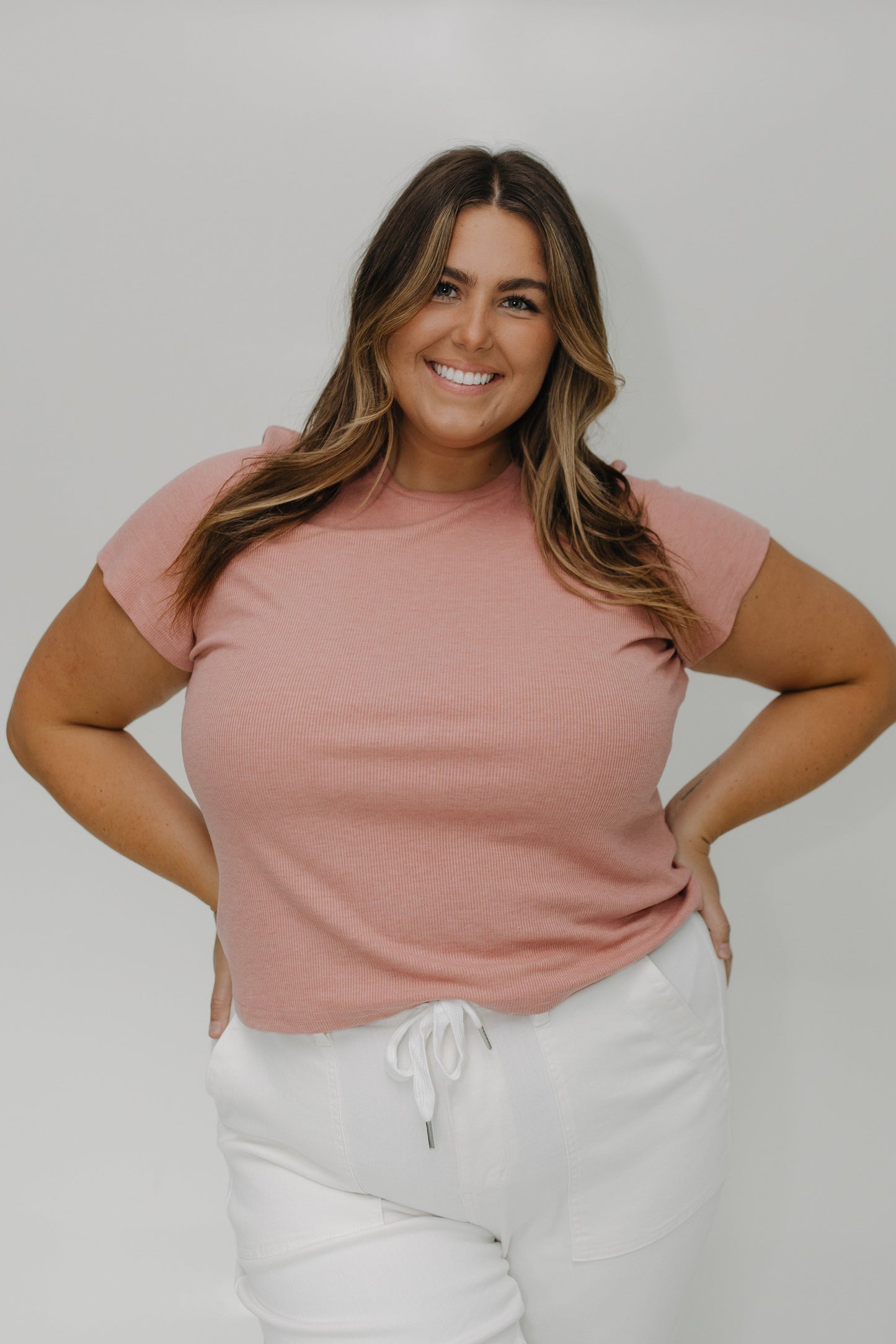 Woman wearing a pink t-shirt and white pants against a plain background