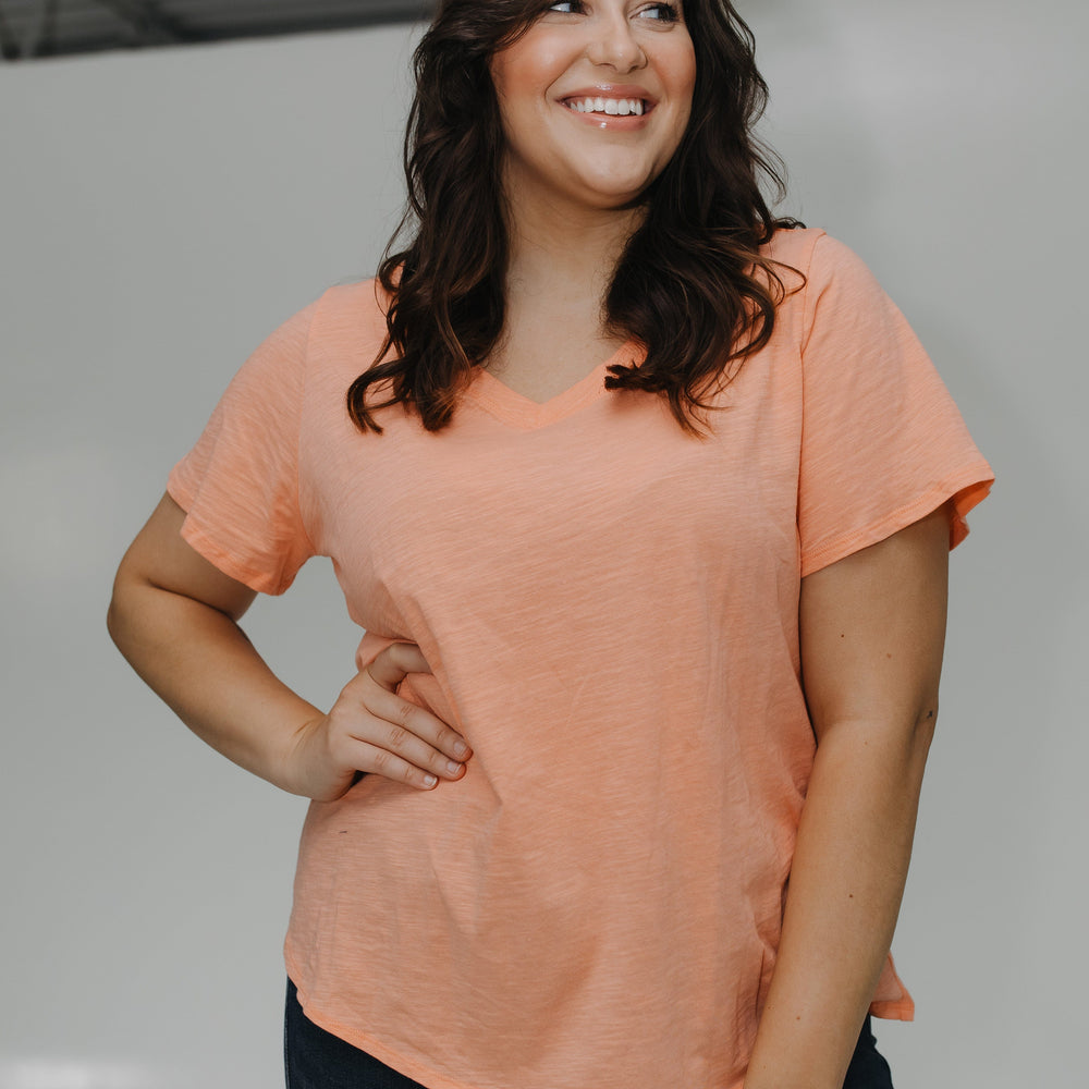 Woman wearing a peach-colored t-shirt and dark pants against a plain background