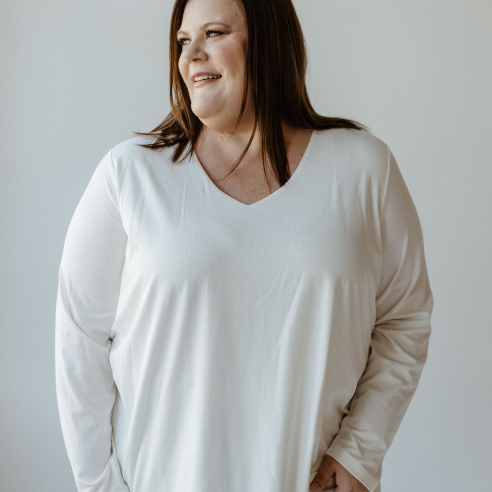 A person with long hair wearing a luxury V-neck blouse in ecru from Yesta and black pants poses against a plain light background.