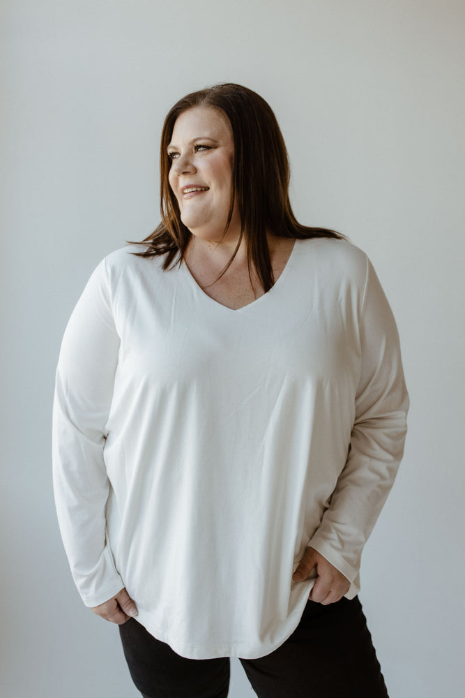 A person with long hair wearing a luxury V-neck blouse in ecru from Yesta and black pants poses against a plain light background.