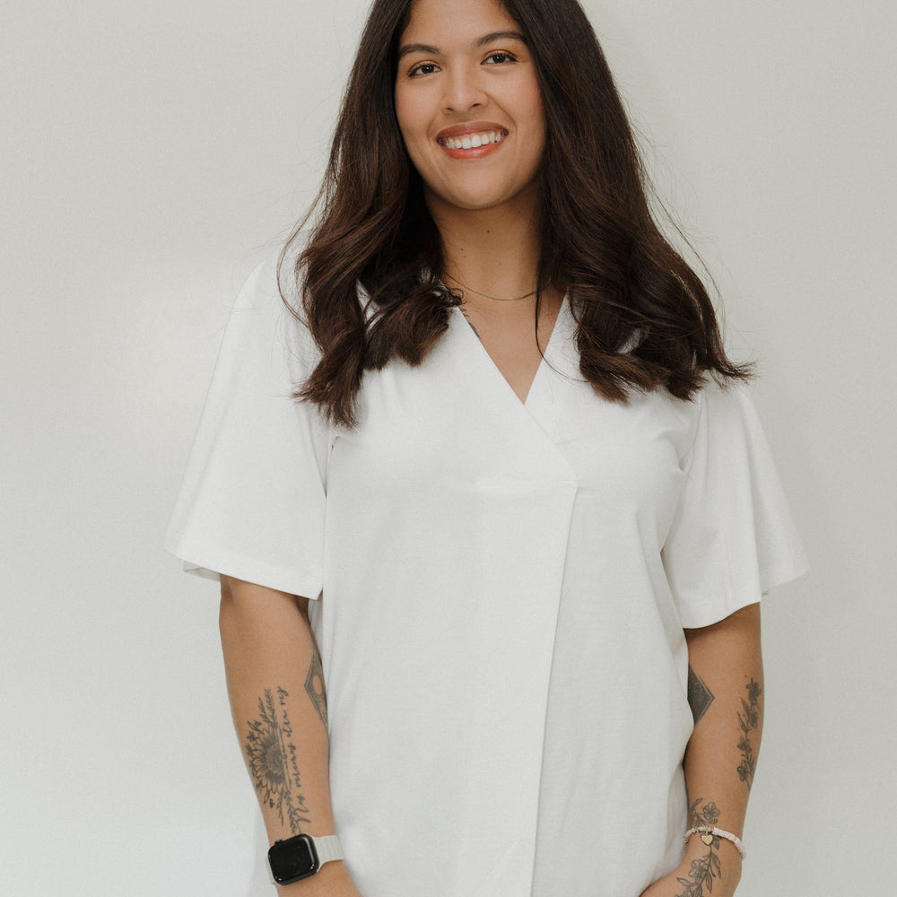 Woman wearing a white blouse with tattoos on her arms against a plain background