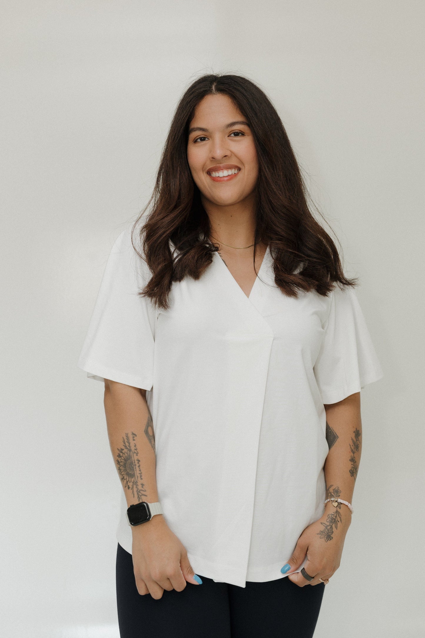 Woman wearing a white blouse with tattoos on her arms against a plain background
