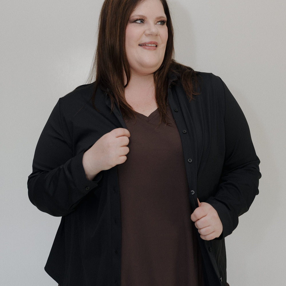 Woman wearing a black cardigan over a brown shirt against a plain background