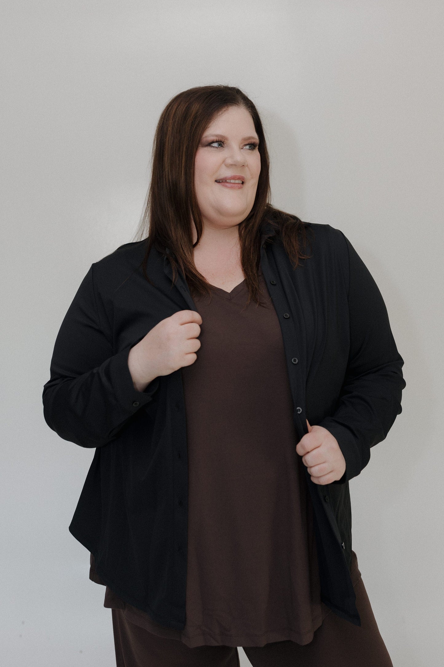 Woman wearing a black cardigan over a brown shirt against a plain background