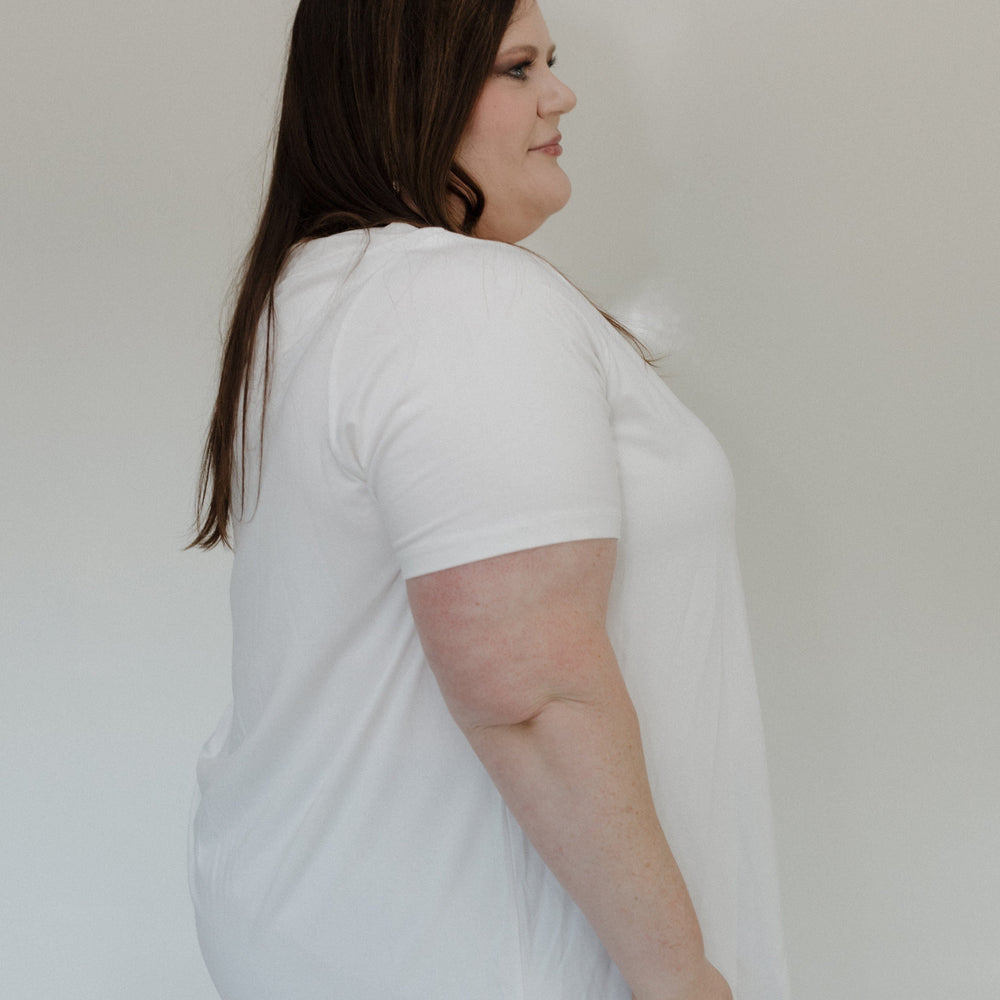 Woman wearing a white t-shirt and gray pants against a plain background