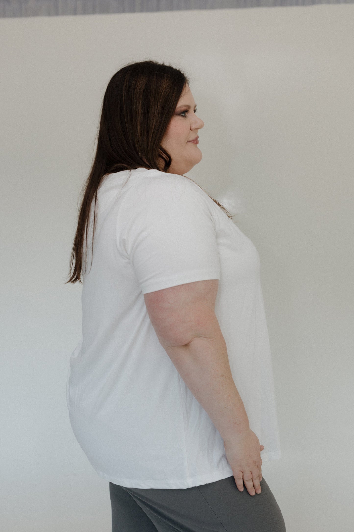 Woman wearing a white t-shirt and gray pants against a plain background