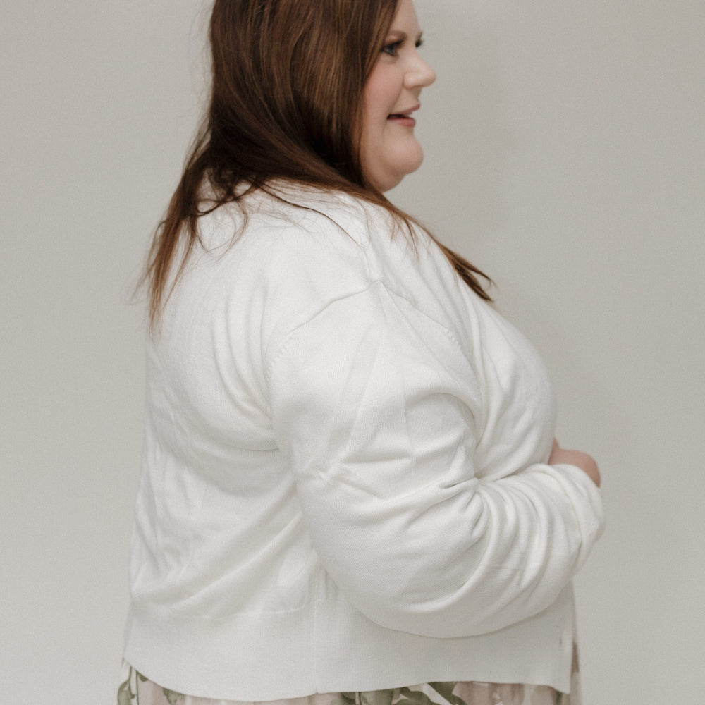 Woman wearing a white cardigan over a floral dress against a plain background