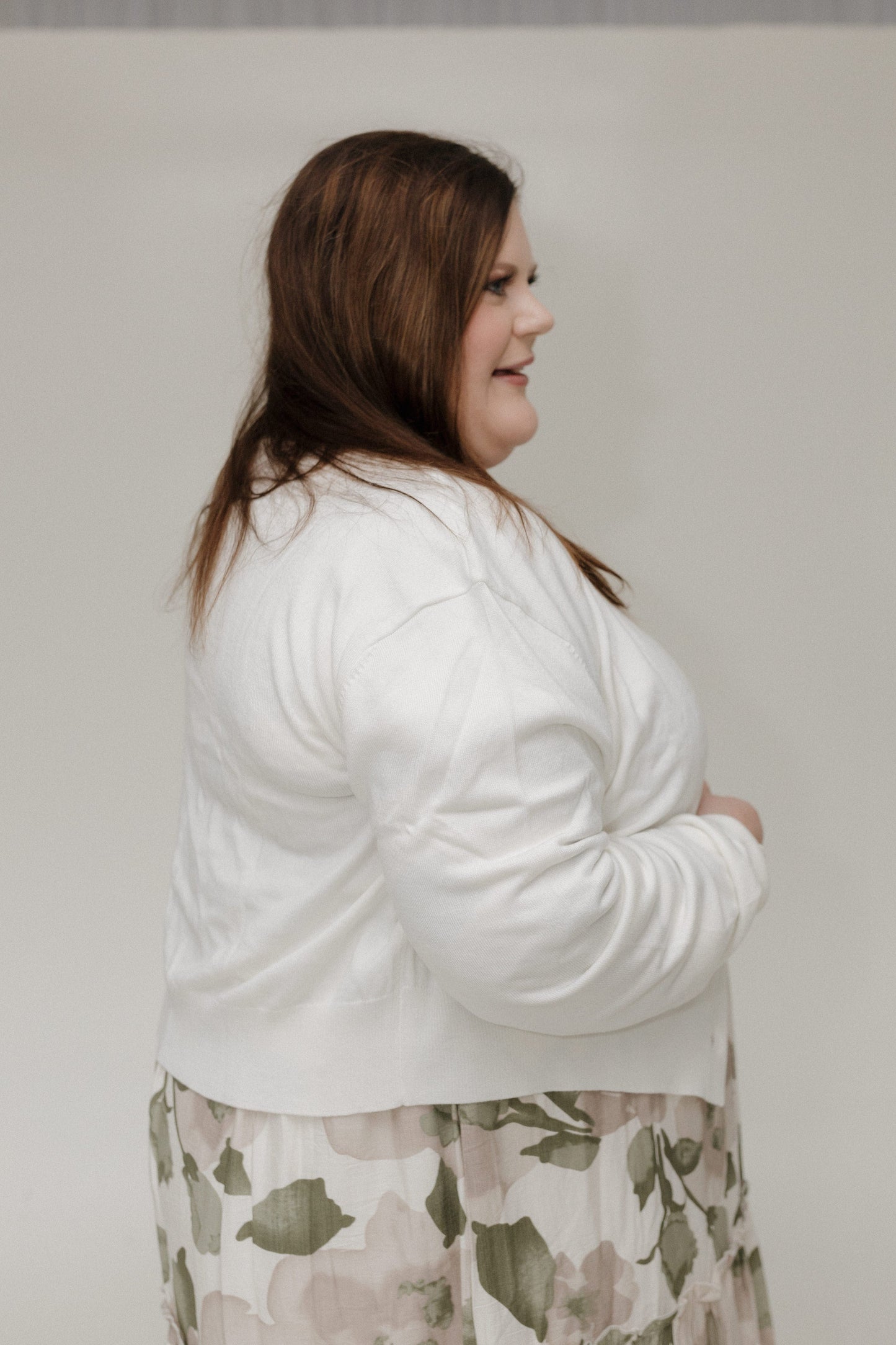 Woman wearing a white cardigan over a floral dress against a plain background