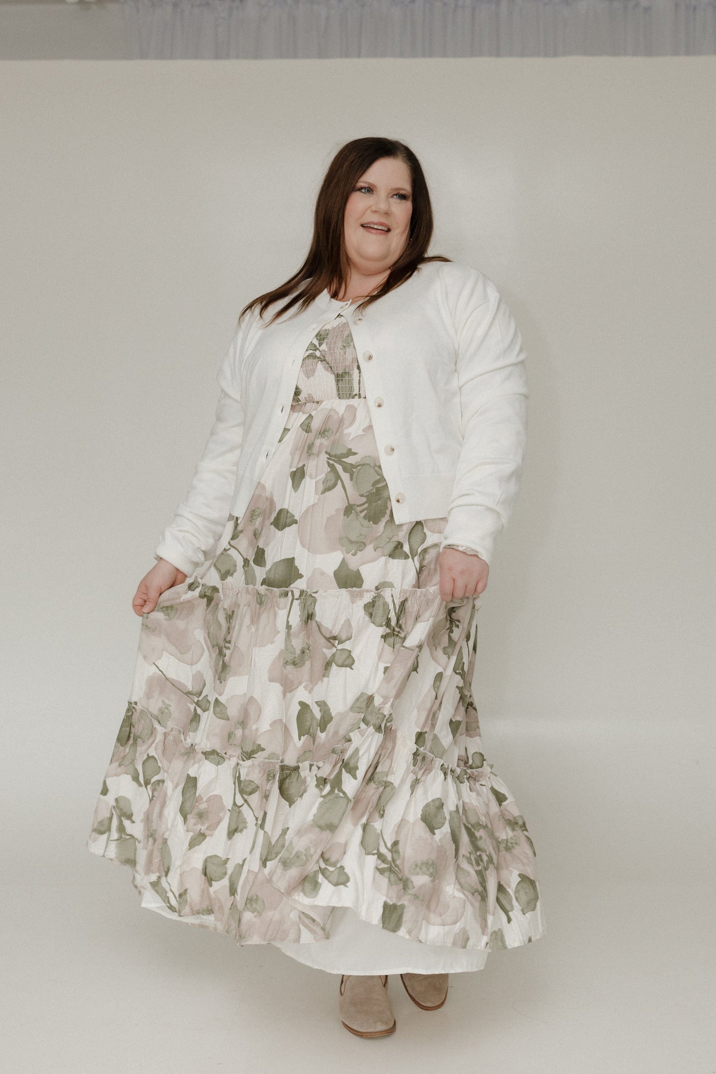 Woman wearing a floral dress and white cardigan on a plain background