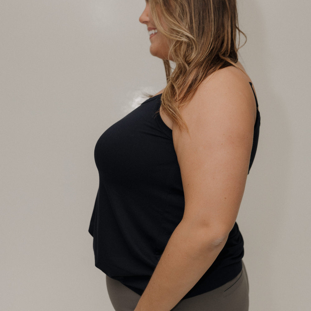Woman wearing a black sleeveless top and gray pants against a plain background