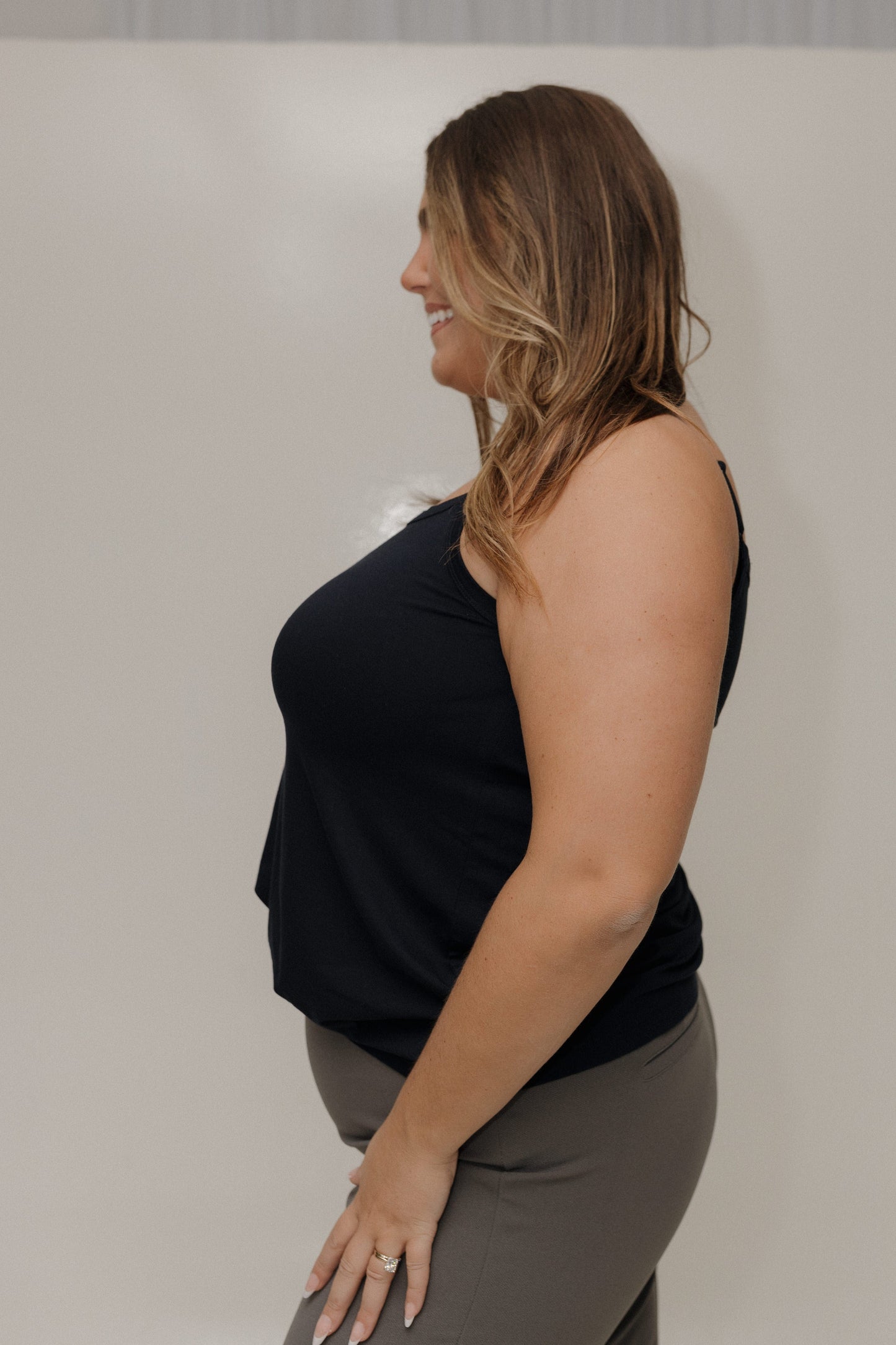 Woman wearing a black sleeveless top and gray pants against a plain background