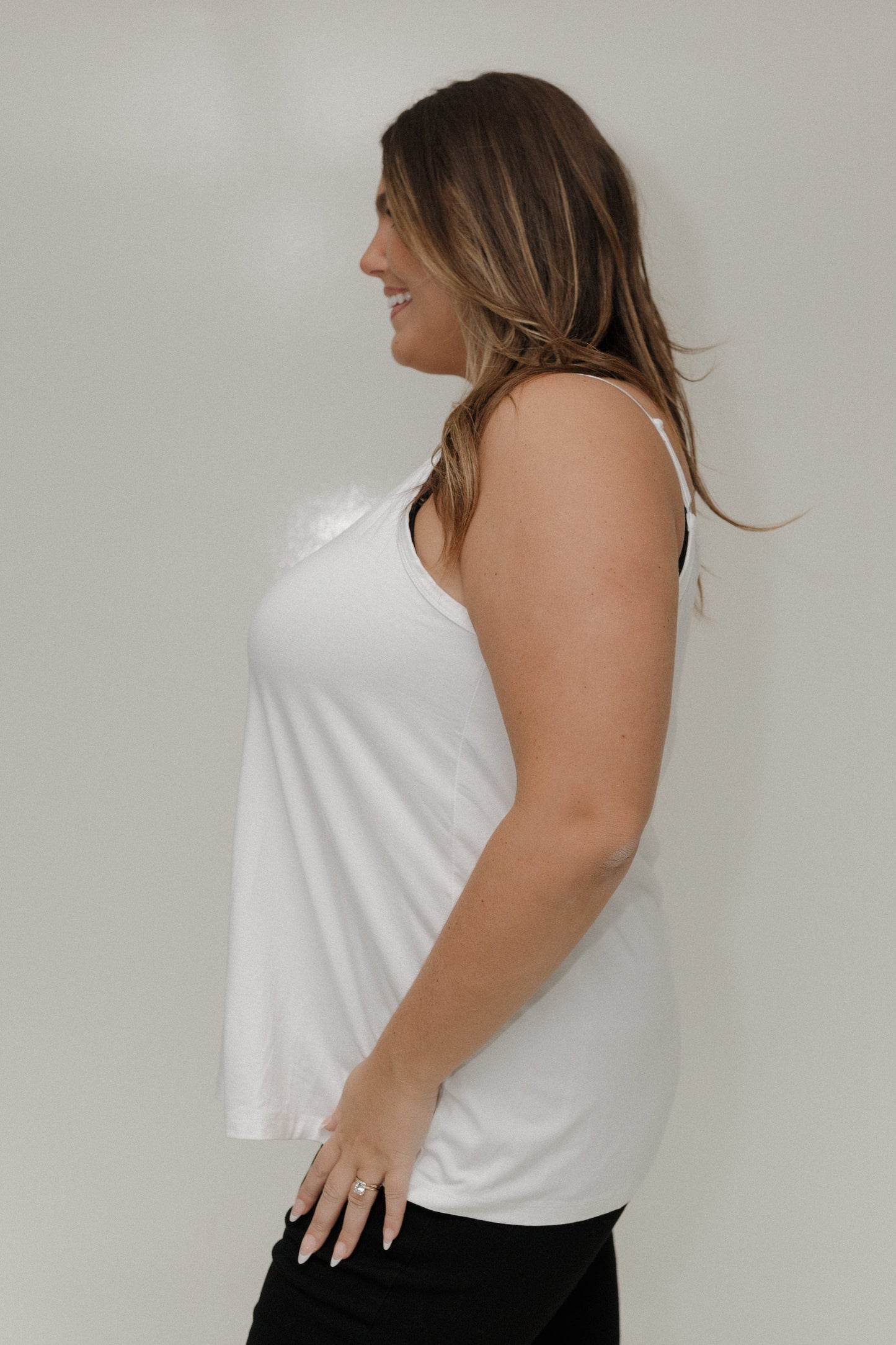 Woman wearing a white sleeveless top against a plain background