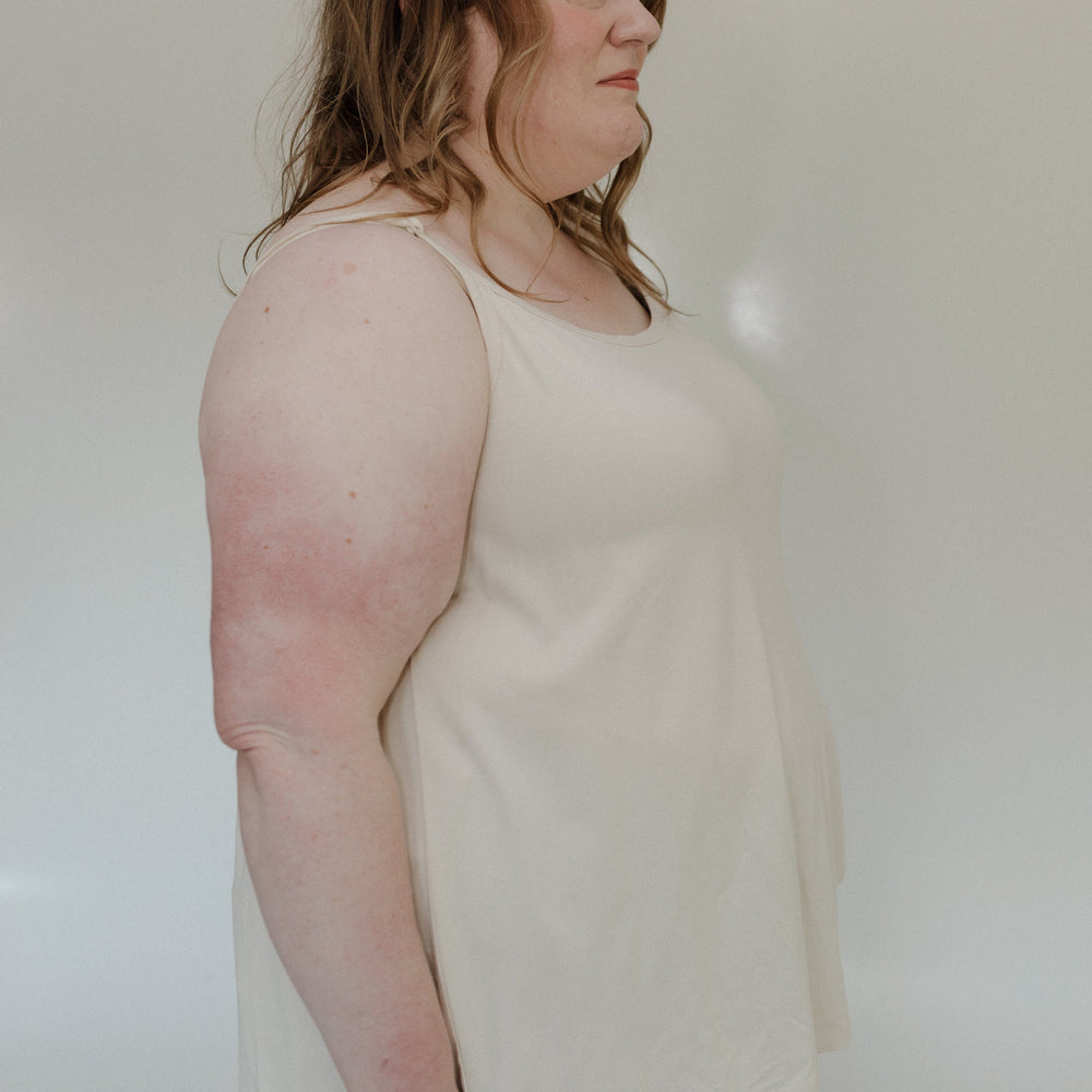 Person wearing a light-colored tank top and jeans against a plain background