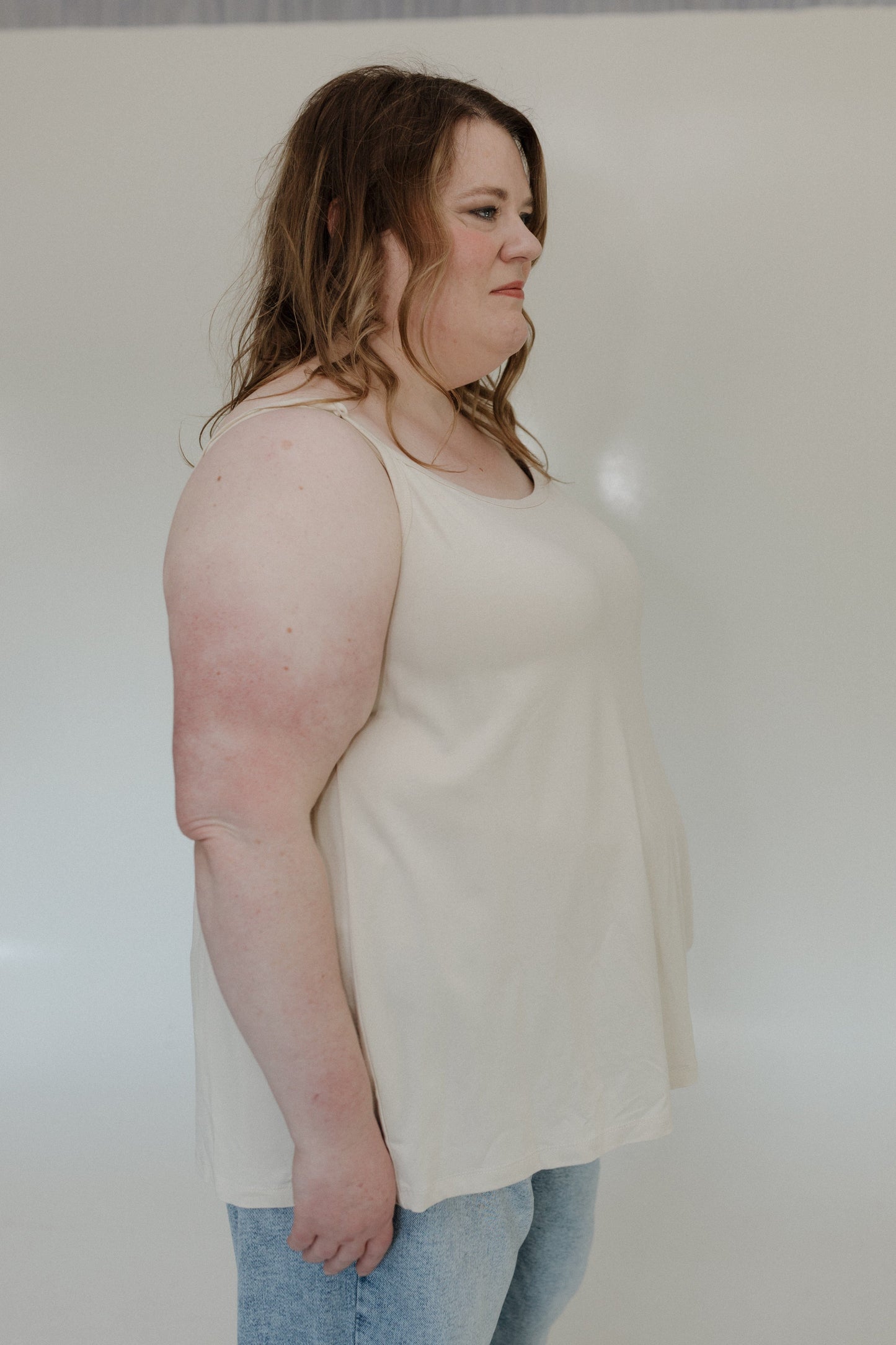 Person wearing a light-colored tank top and jeans against a plain background