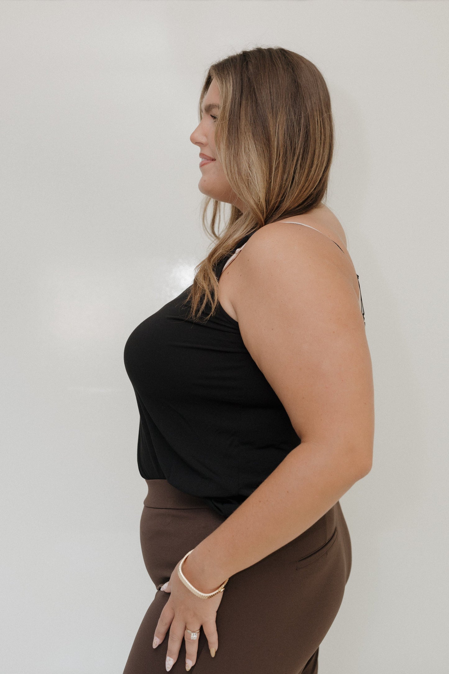 Woman wearing a black top and brown pants against a white background