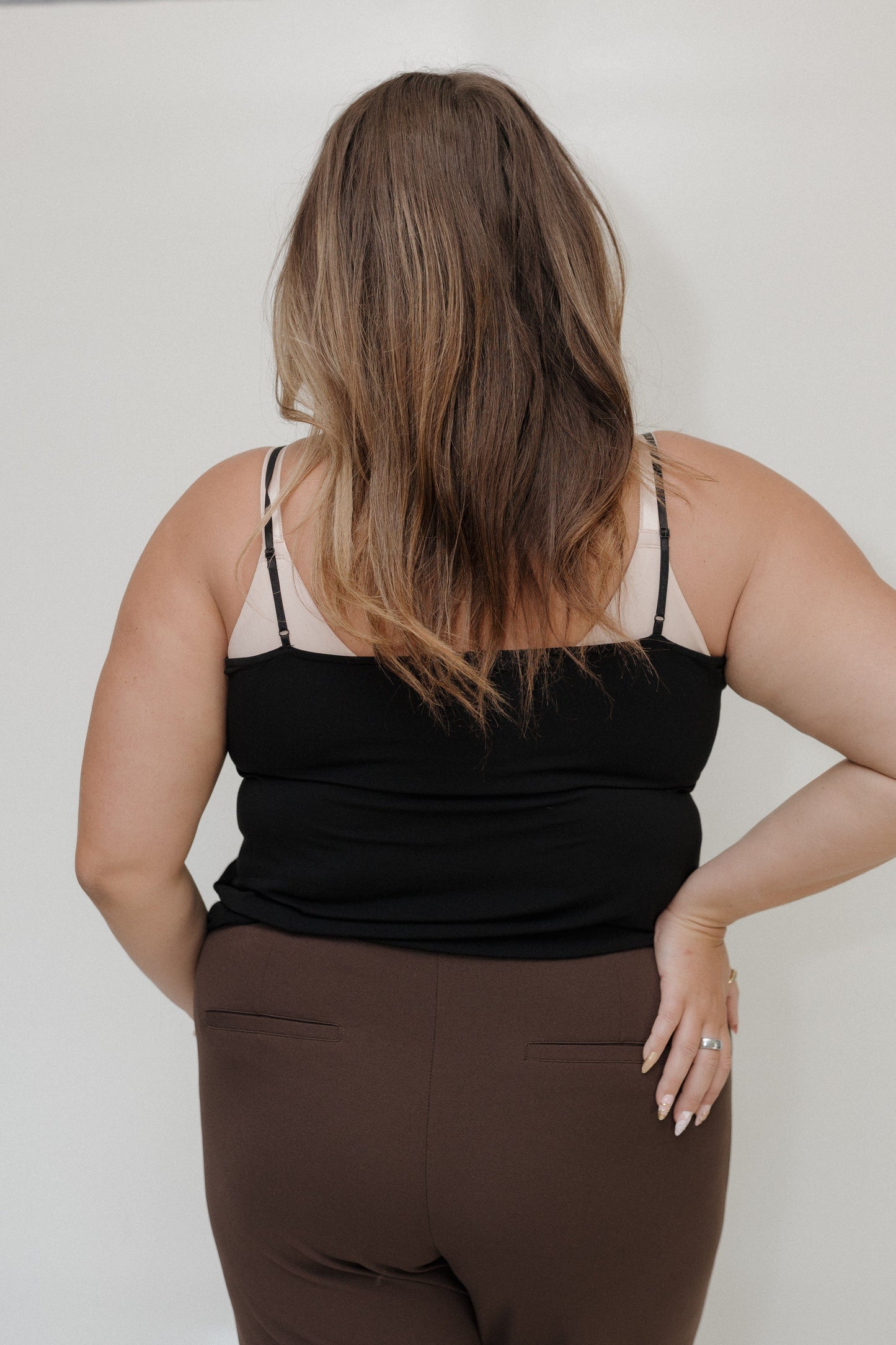 Person wearing a black tank top and brown pants against a plain background