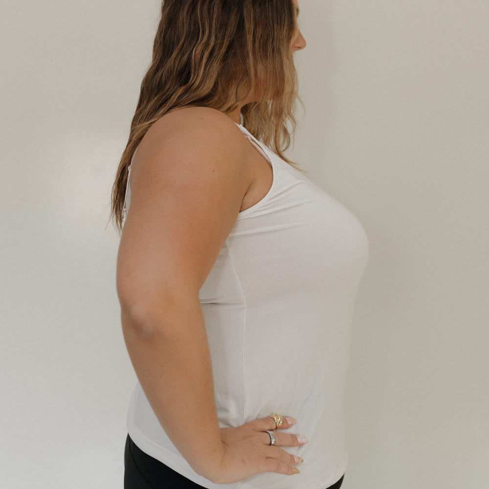 Woman wearing a white tank top and black pants against a plain background