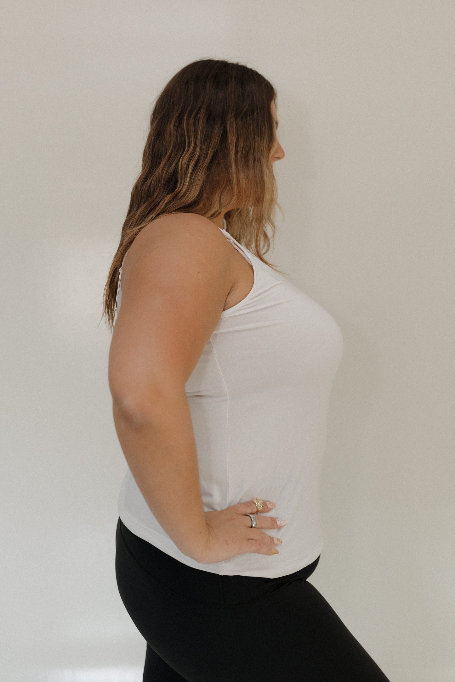 Woman wearing a white tank top and black pants against a plain background