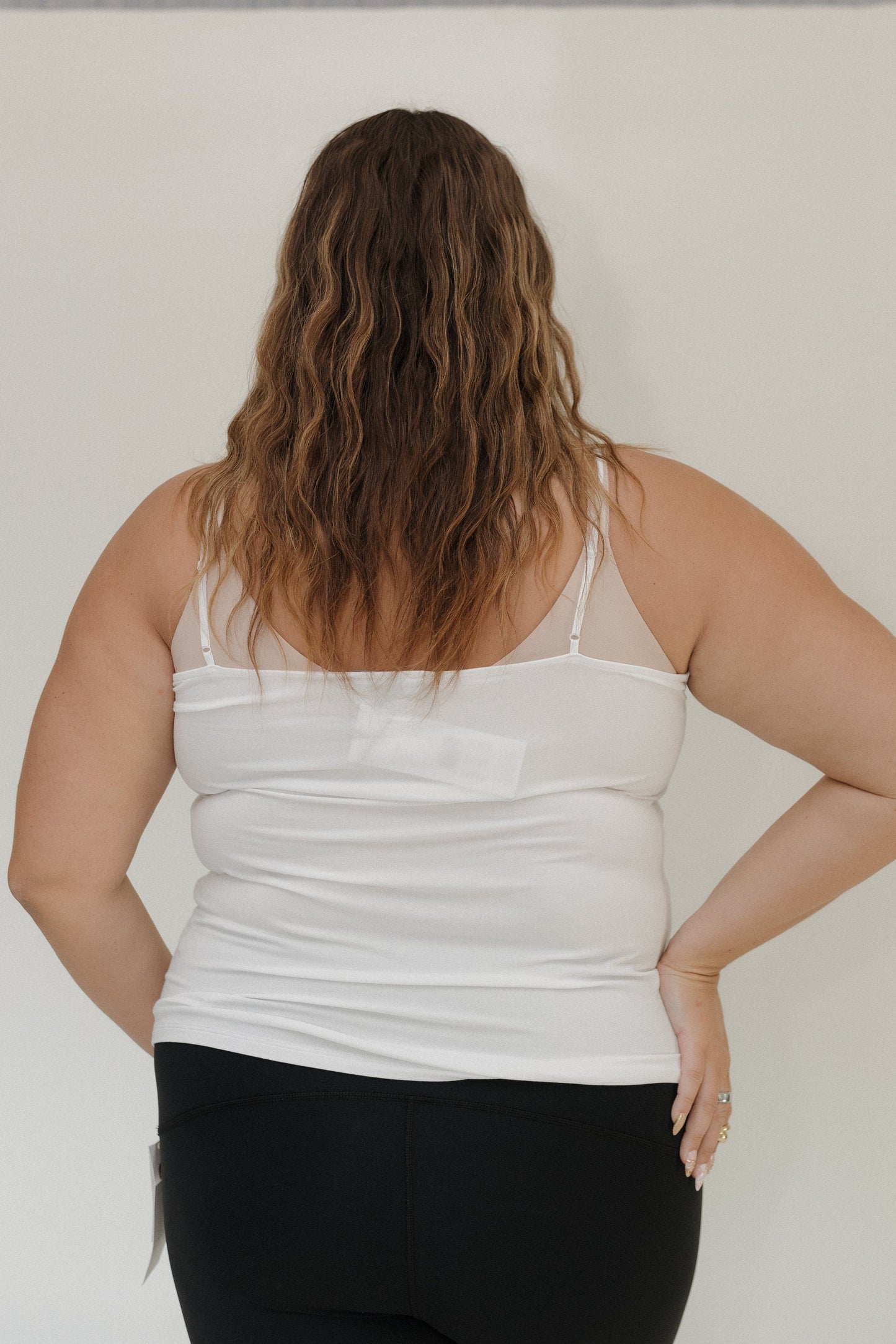 Person wearing a white tank top and black pants against a plain background