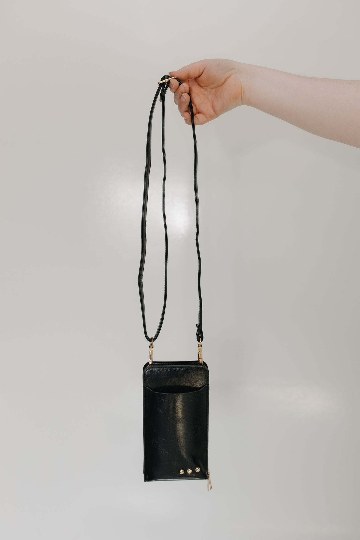 Black leather crossbody bag held by a hand against a light gray background