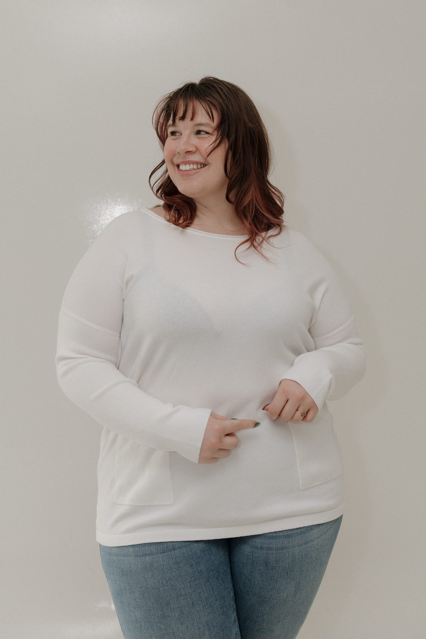 Woman wearing a white sweater and blue jeans against a plain background