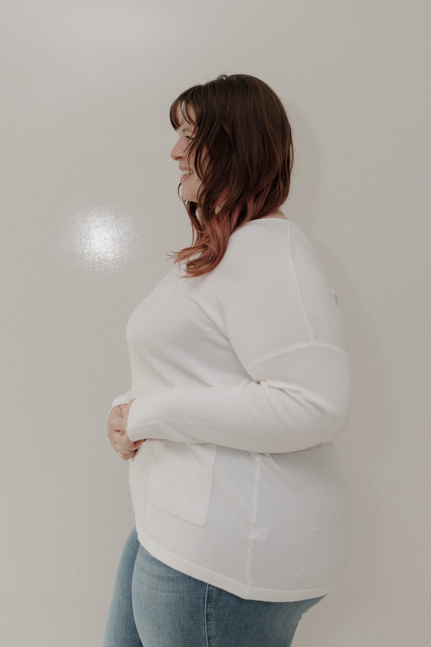 Woman wearing a white sweater and blue jeans against a plain background