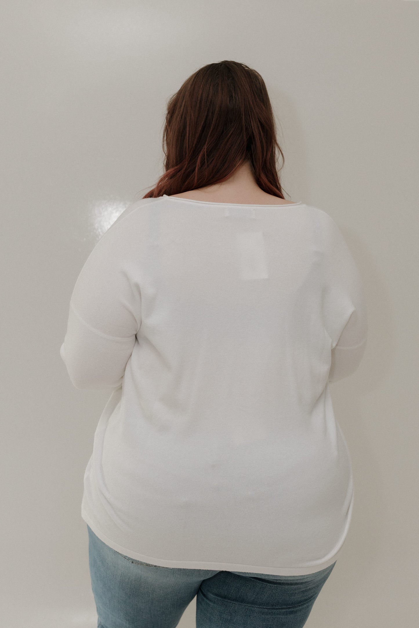 Person wearing a white sweater and blue jeans against a plain background