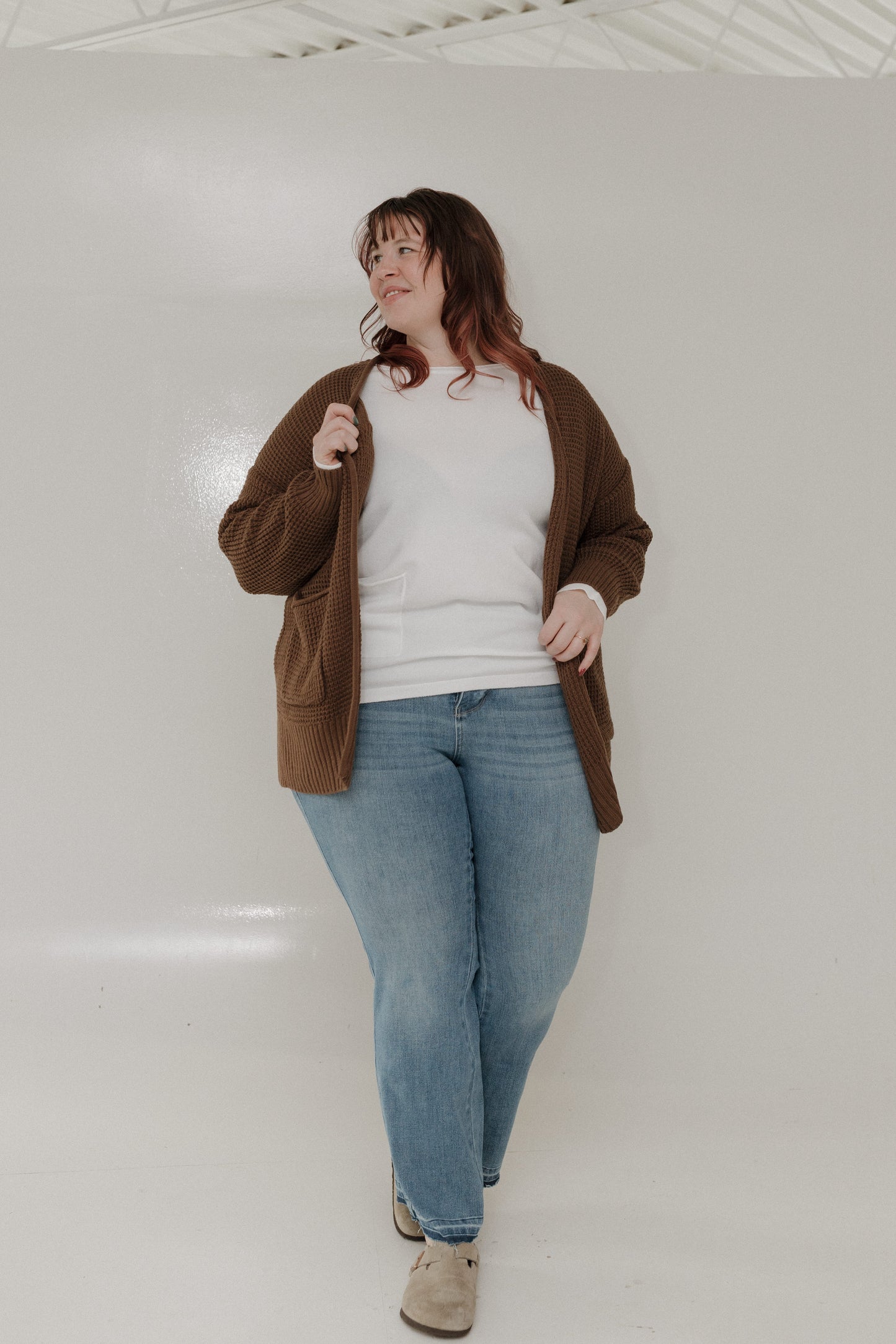 Person wearing a brown jacket, white shirt, and blue jeans against a white background
