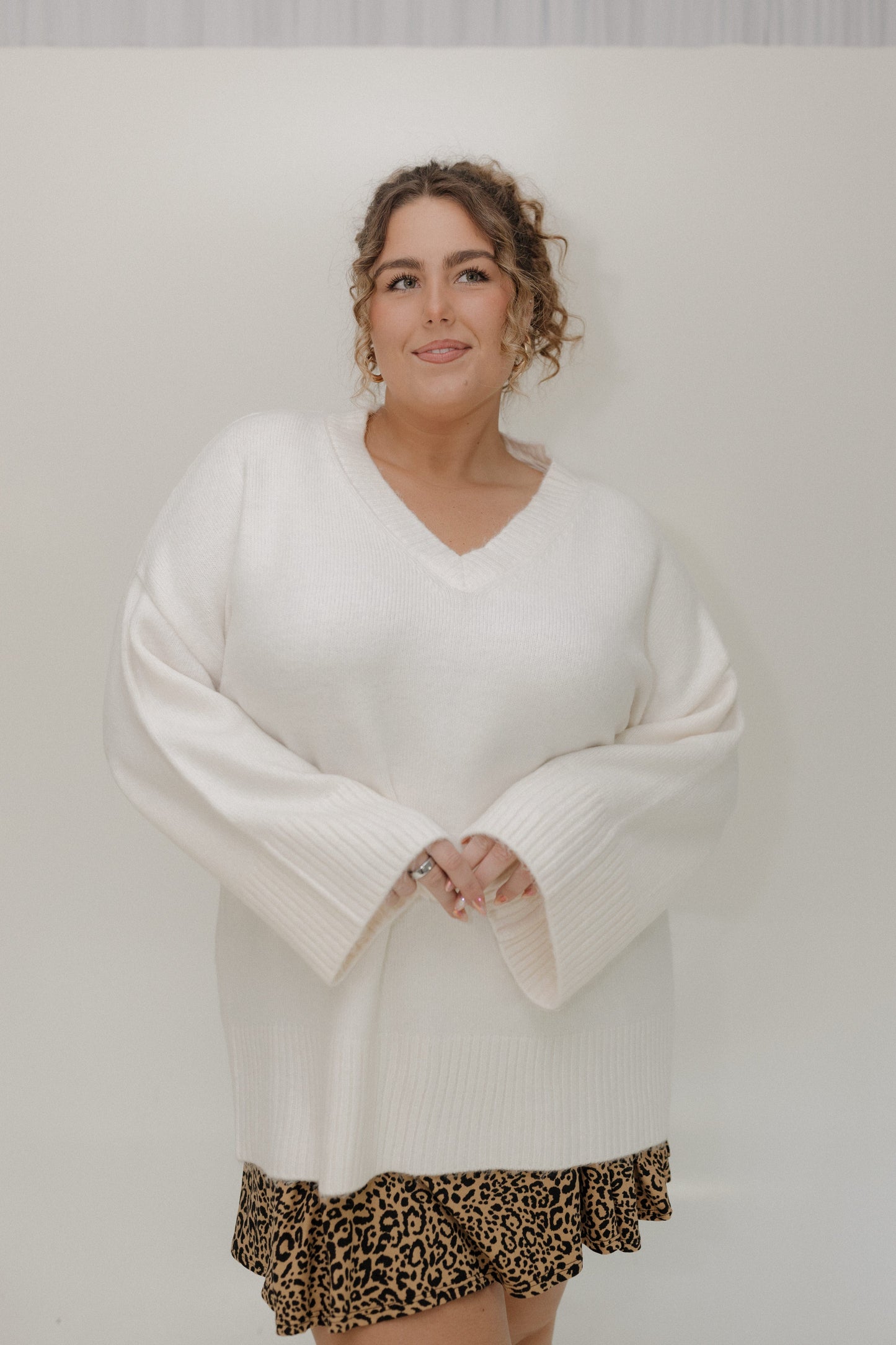 Woman wearing a white sweater and leopard print skirt against a plain background