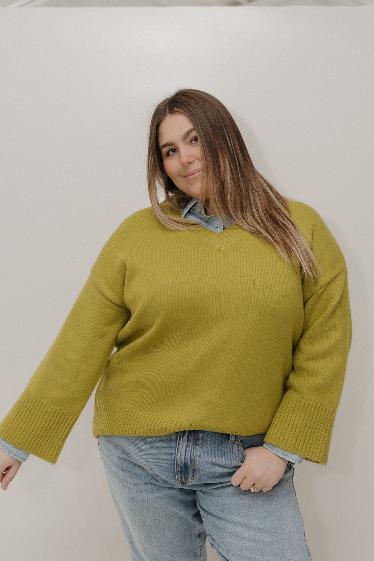 Woman wearing a green sweater and blue jeans against a white background