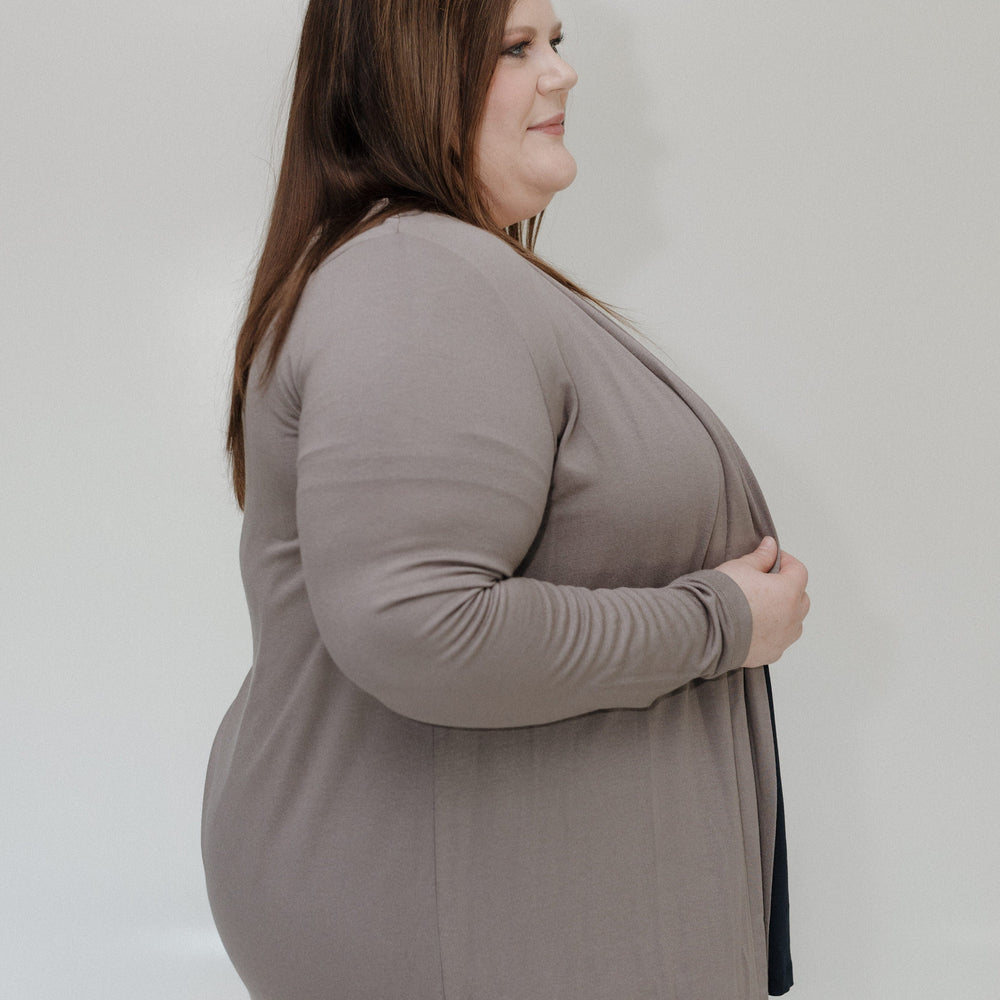 Woman wearing a gray long-sleeve top and beige pants against a plain background