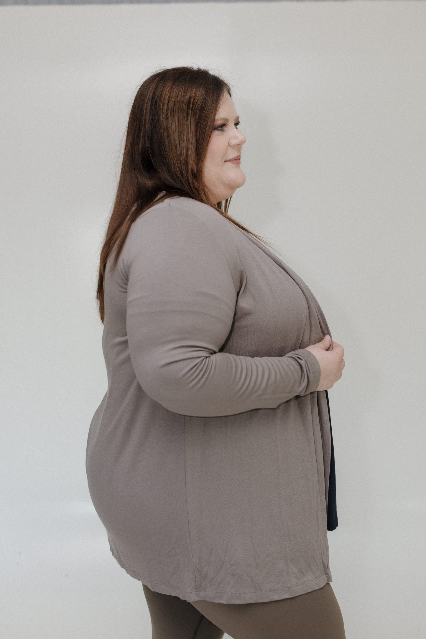 Woman wearing a gray long-sleeve top and beige pants against a plain background