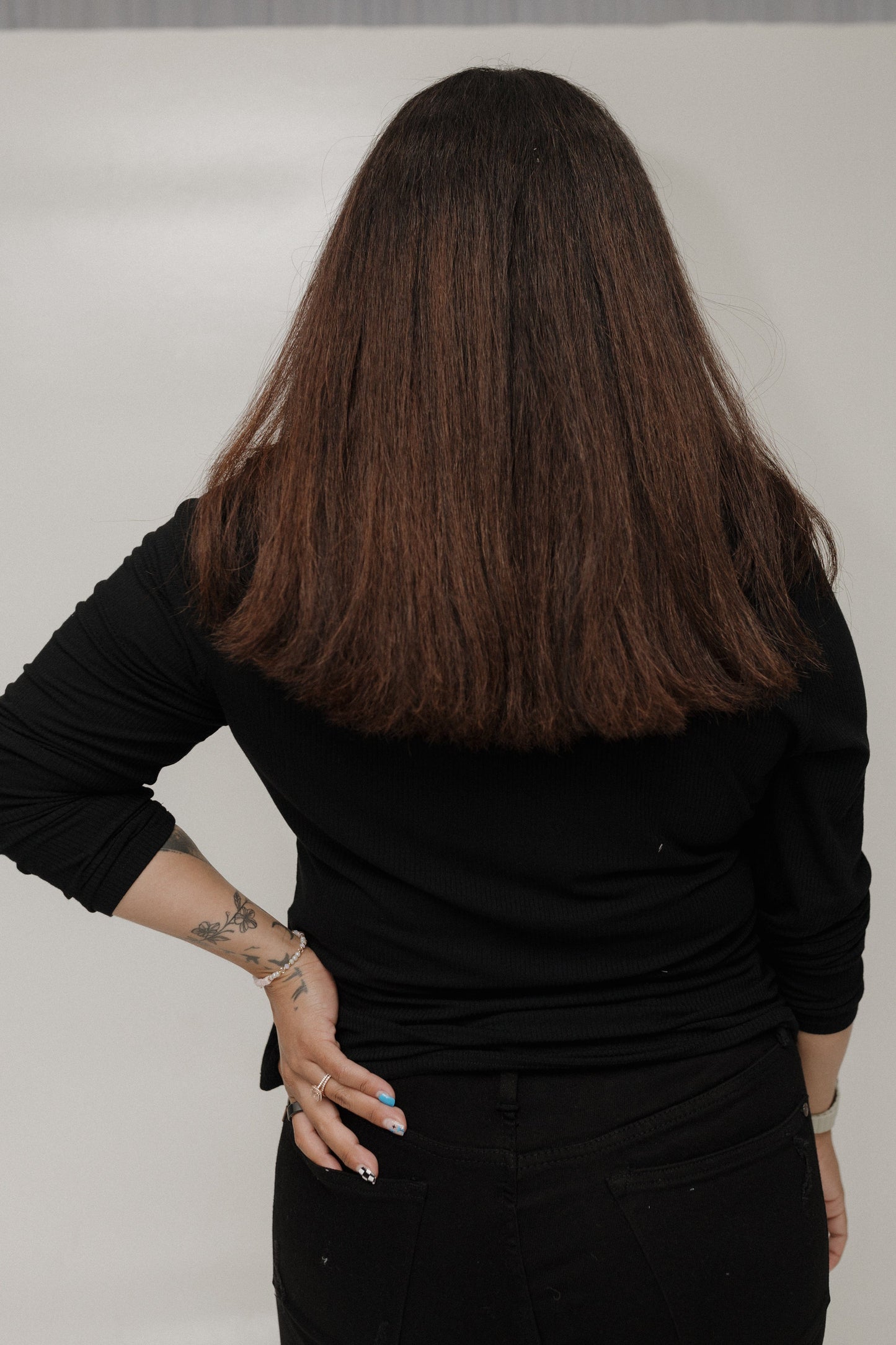 Person with long dark hair wearing a black outfit against a plain background