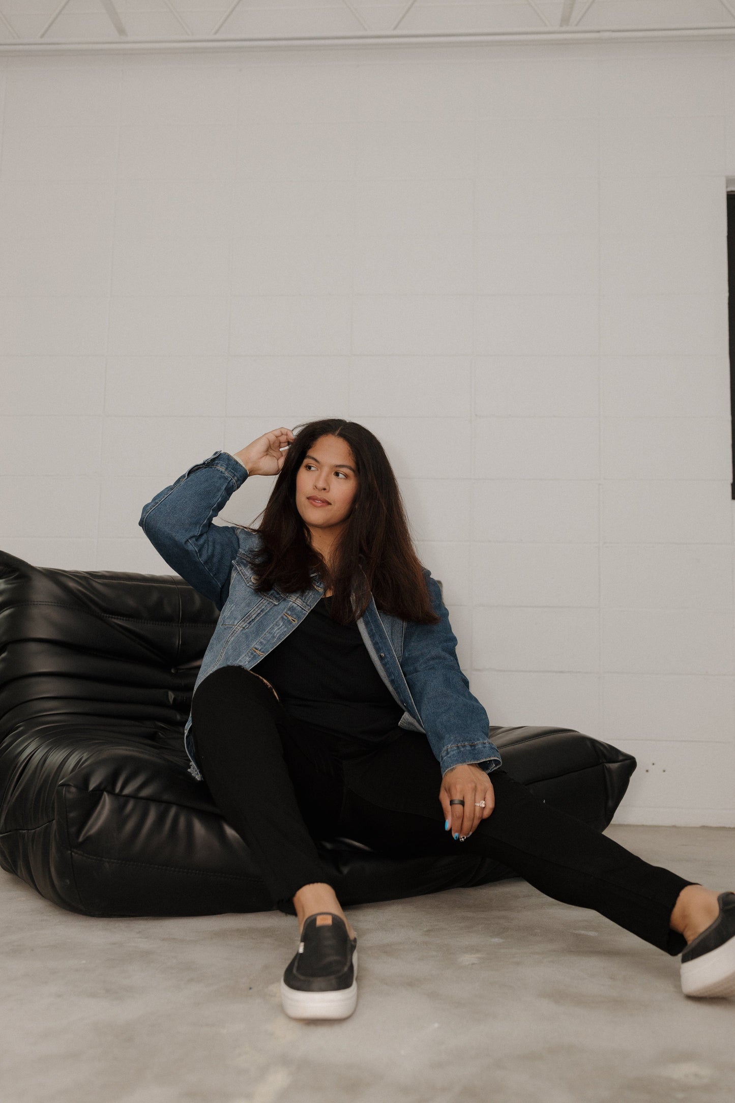 Woman sitting on a black leather couch against a white wall