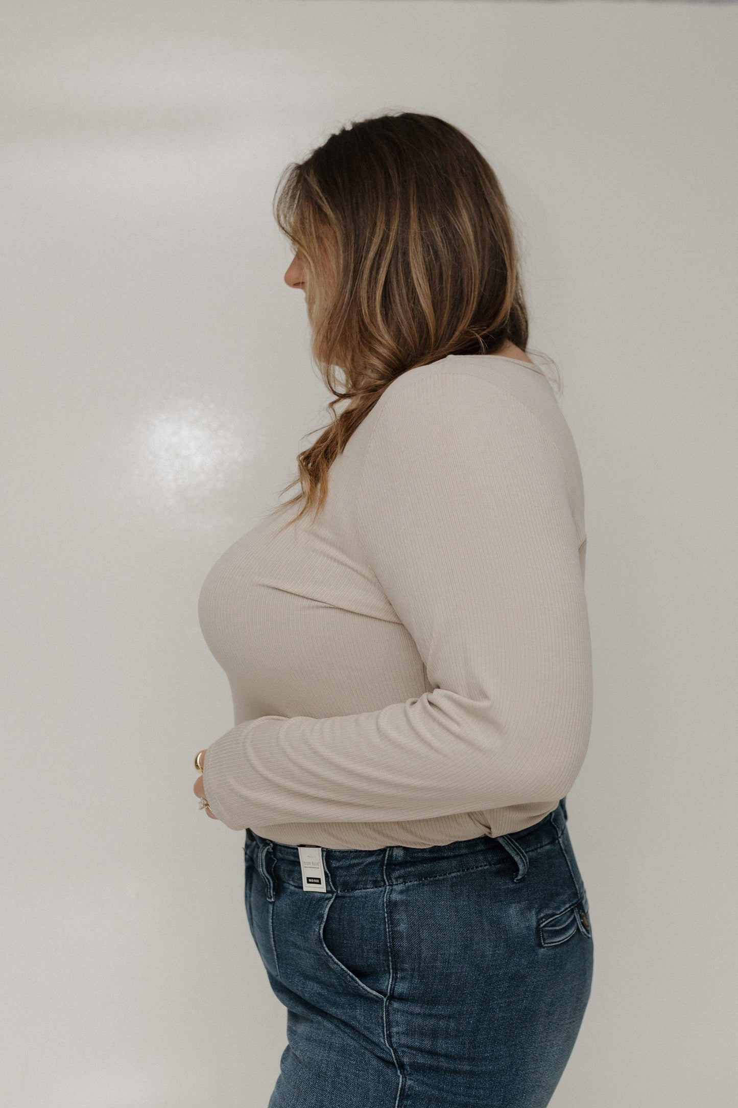 Person wearing a beige long-sleeve top and blue jeans against a plain background
