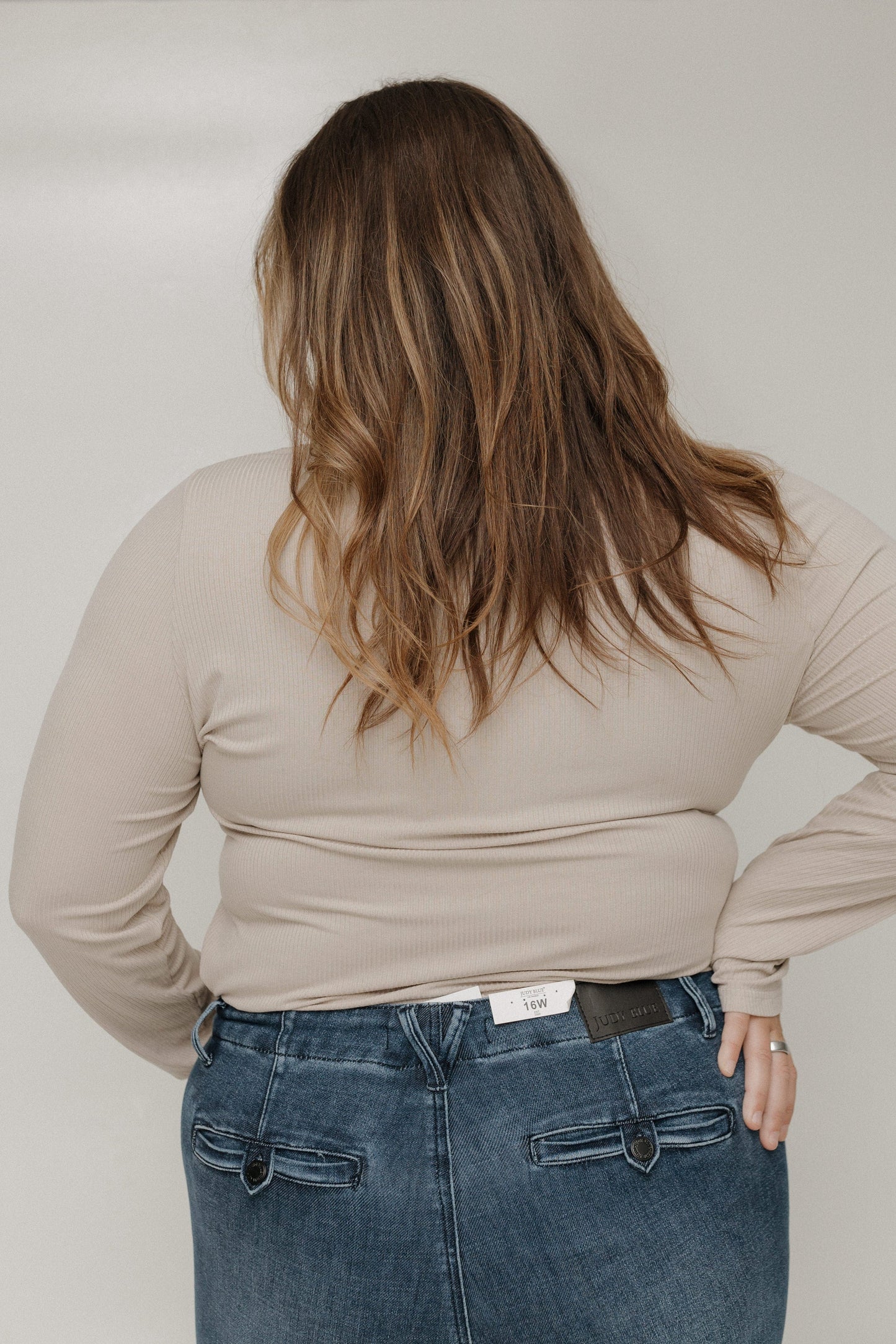 Person wearing a beige long-sleeve top and blue jeans against a plain background