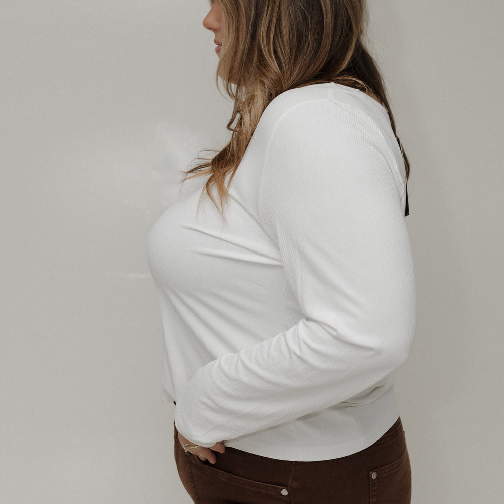 Person wearing a white long-sleeve shirt and brown pants against a plain background