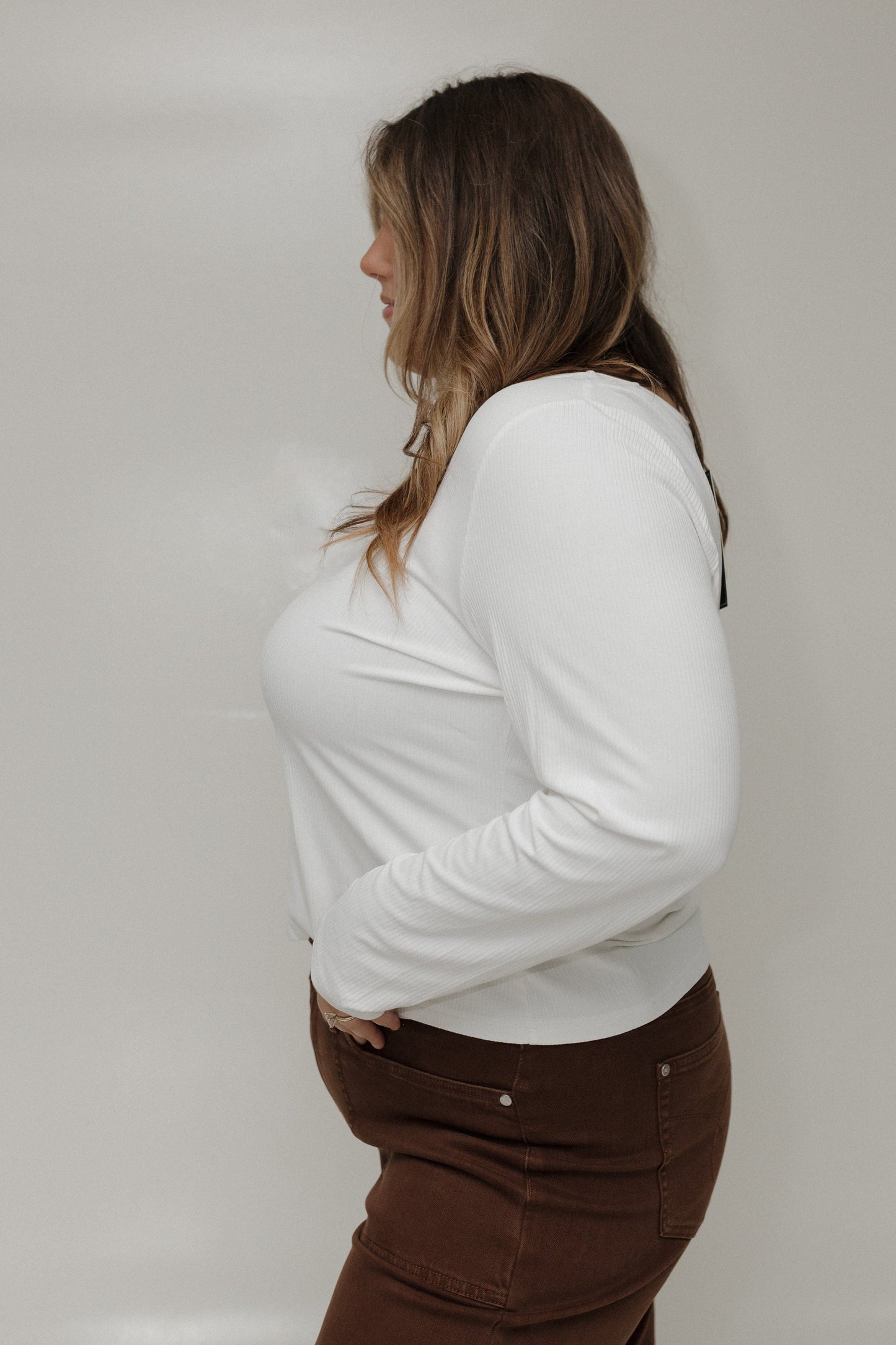 Person wearing a white long-sleeve shirt and brown pants against a plain background
