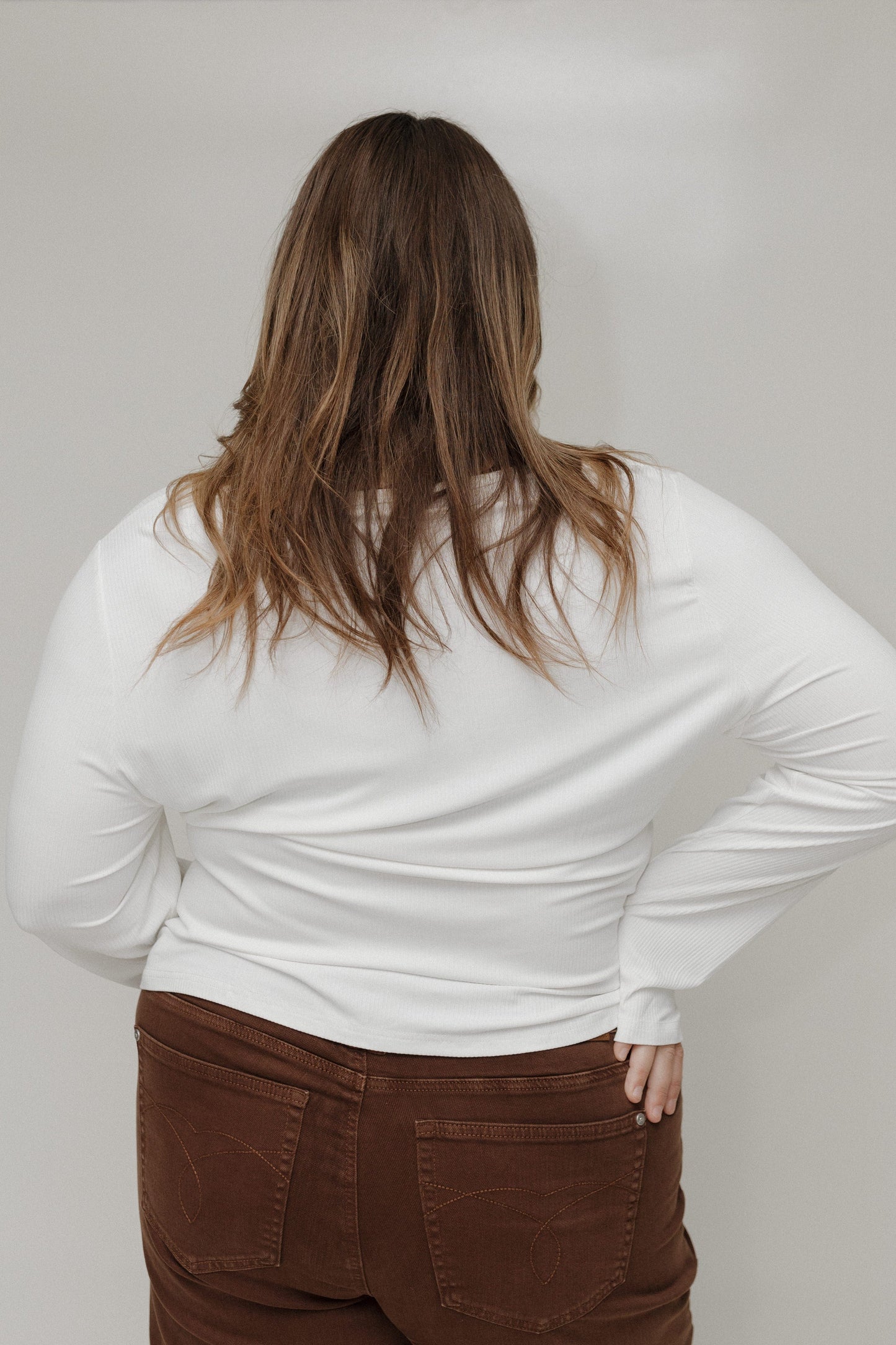 Person wearing a white long-sleeve shirt and brown pants against a plain background
