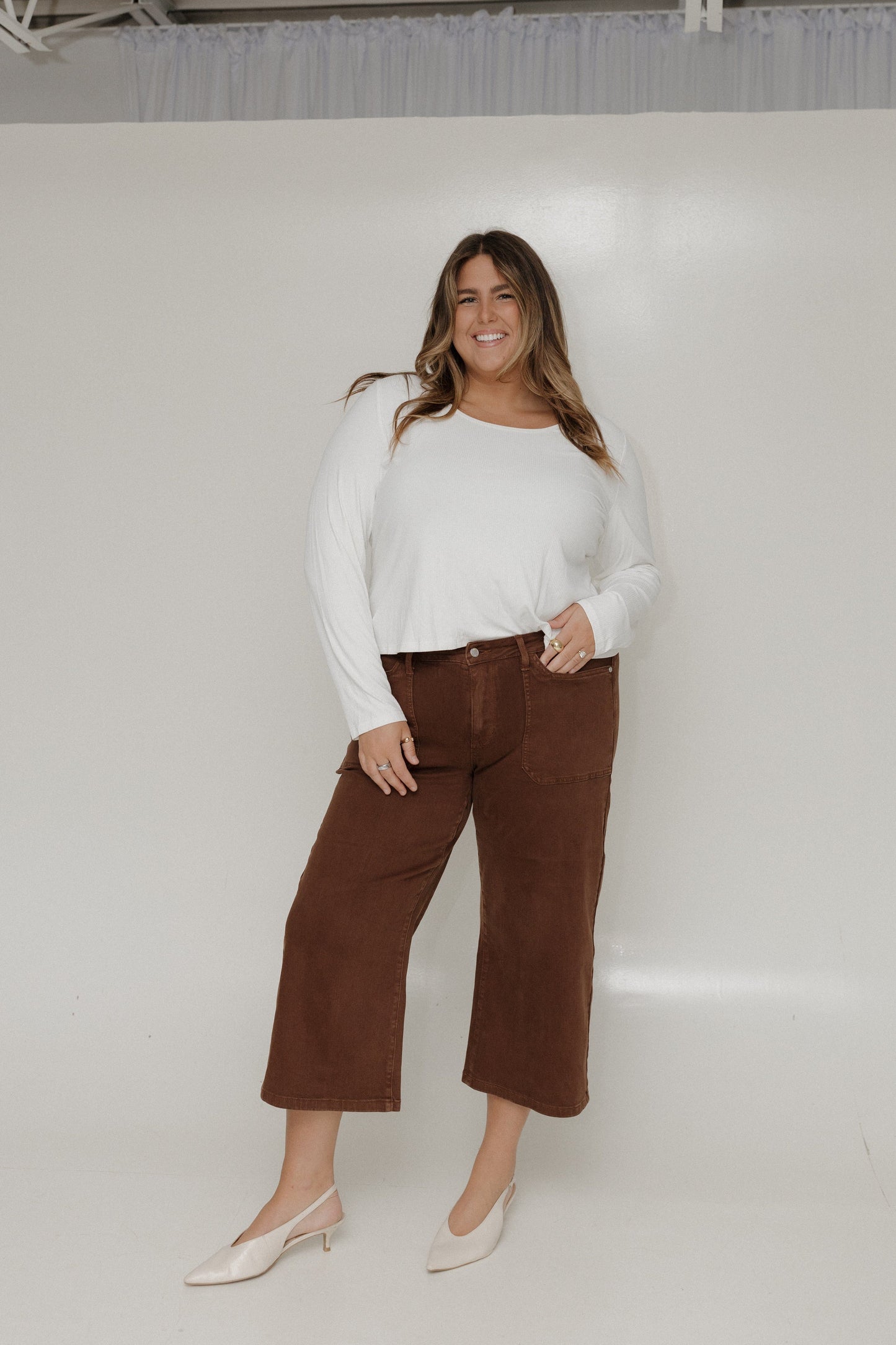 Woman wearing a white top and brown pants against a white background