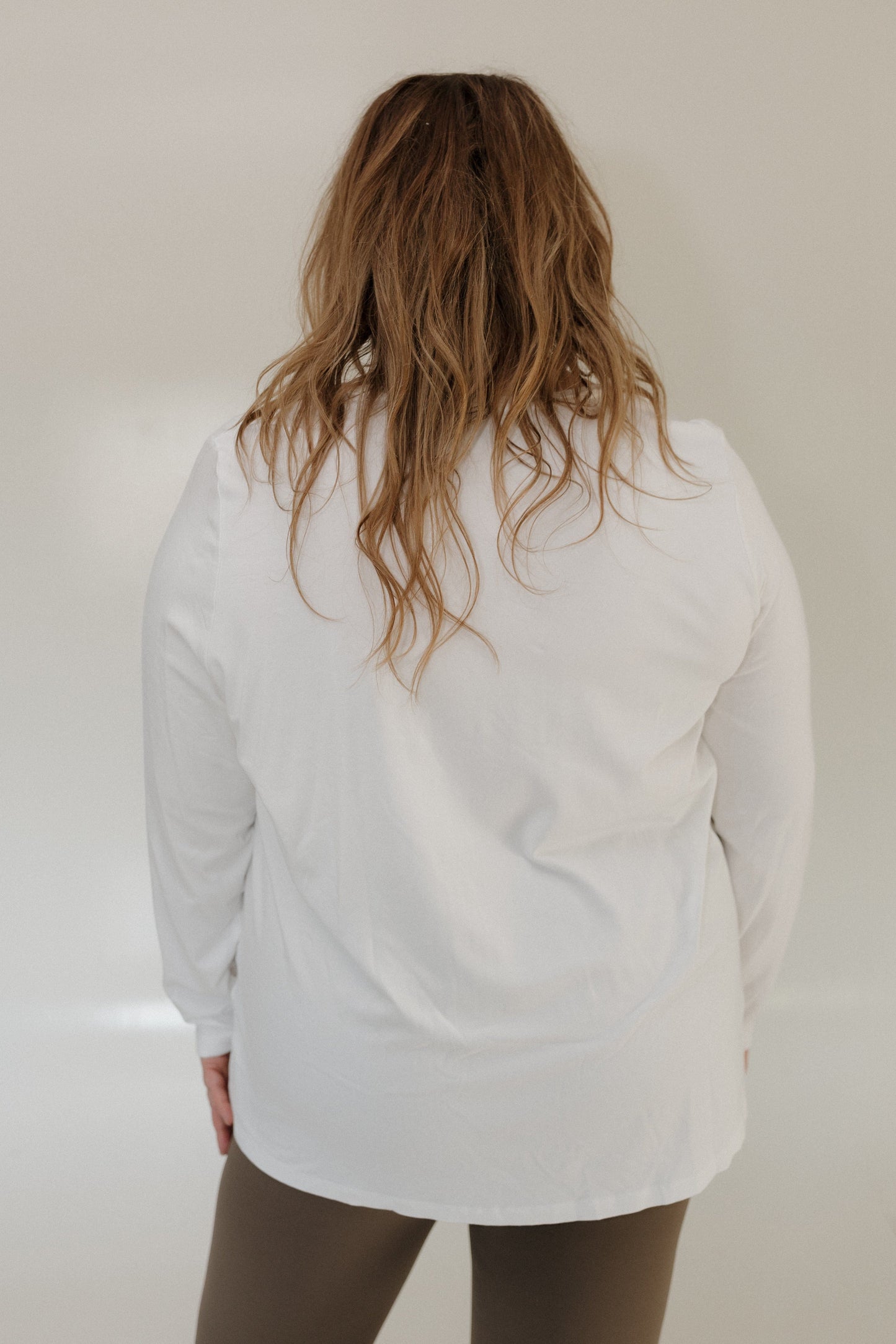 Person wearing a white long-sleeve shirt against a plain background