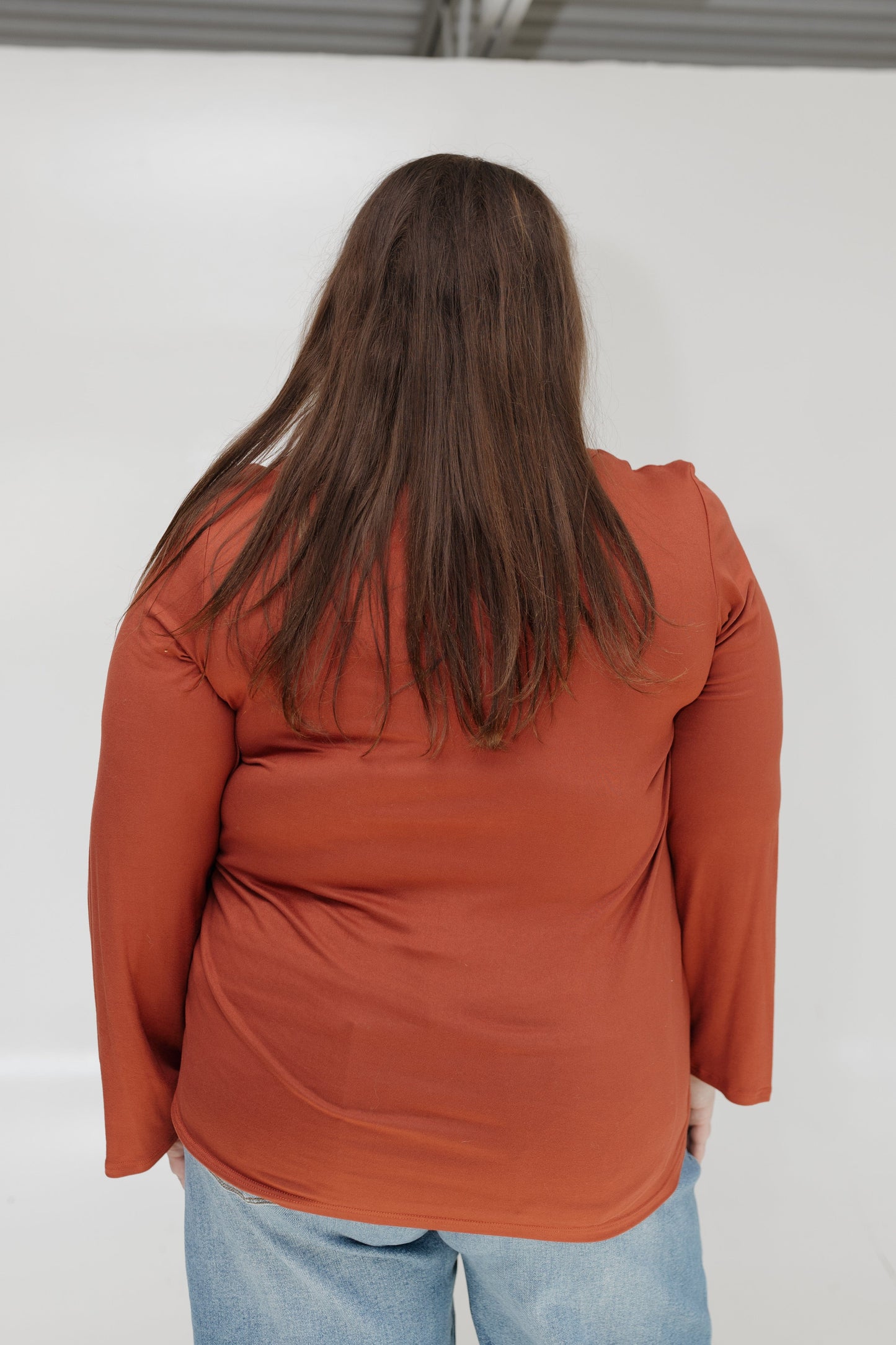 Person wearing a rust-colored long-sleeve shirt against a white background
