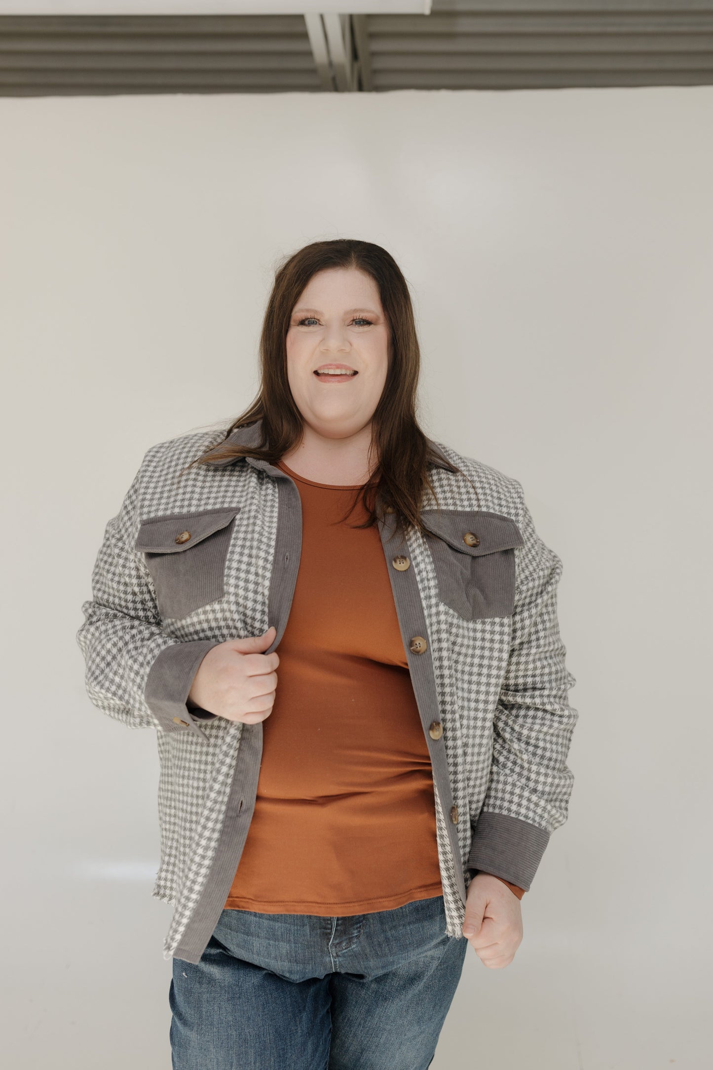 Person wearing a plaid jacket over a brown shirt and jeans against a plain background
