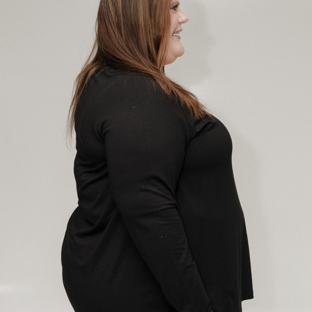 Woman wearing a black top and blue jeans against a plain background