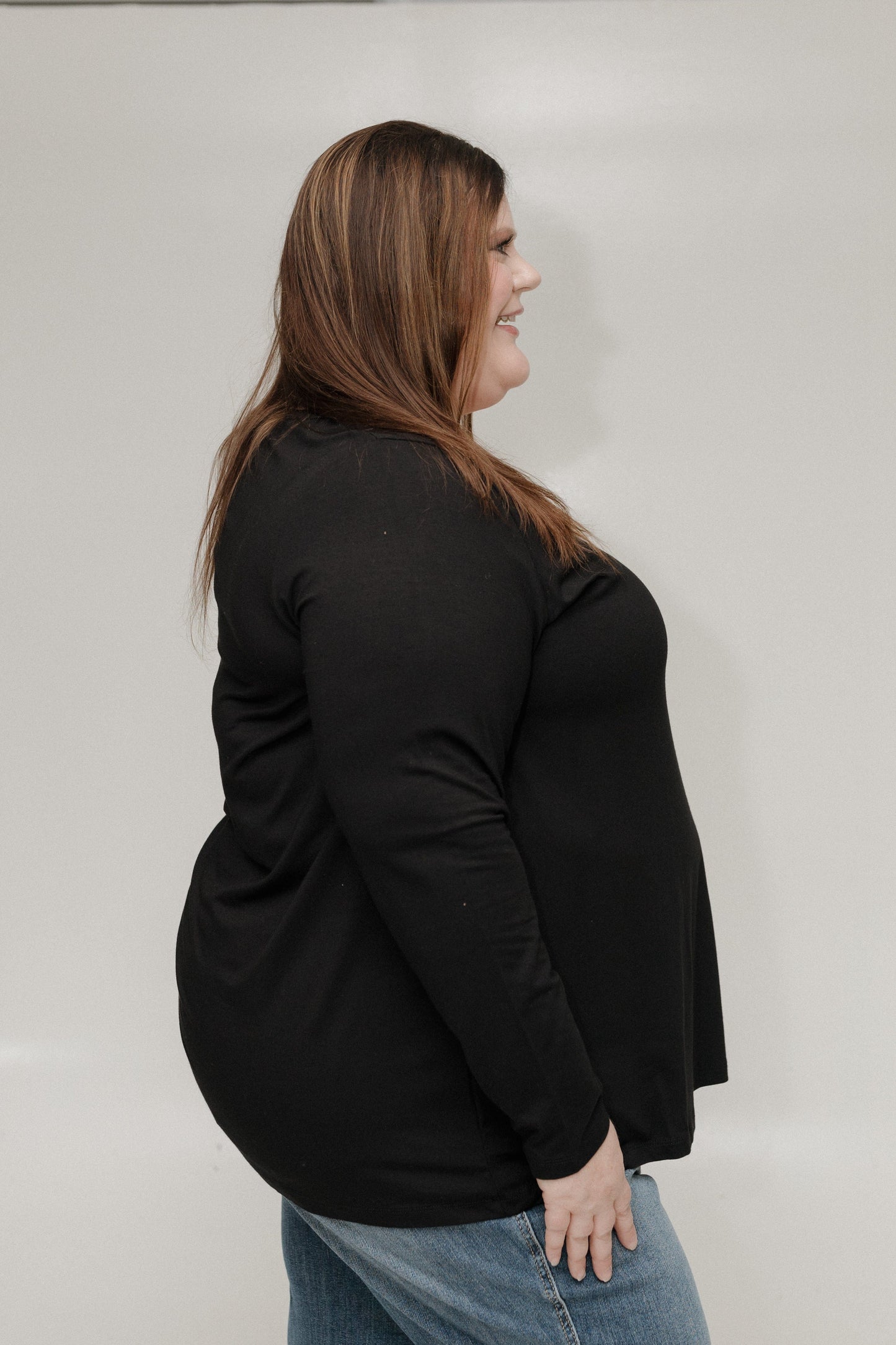 Woman wearing a black top and blue jeans against a plain background