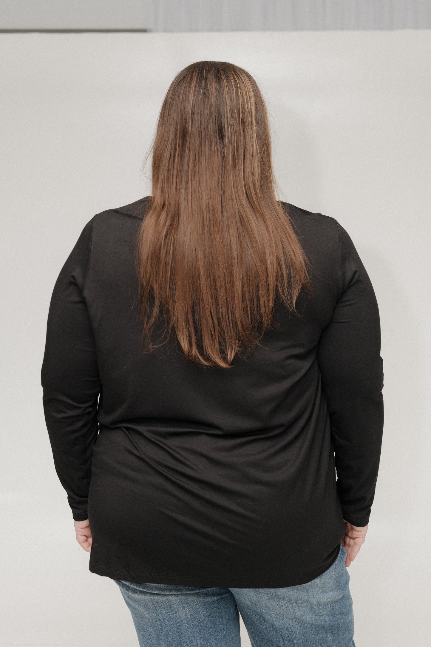 Person wearing a black long-sleeve shirt and blue jeans against a plain background